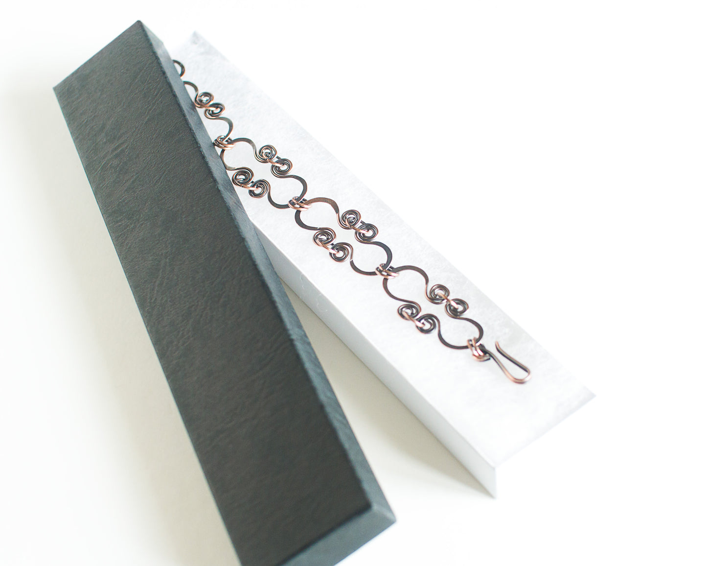 Copper Bracelet with hoop-shaped links in a black box with a white interior on a white background.