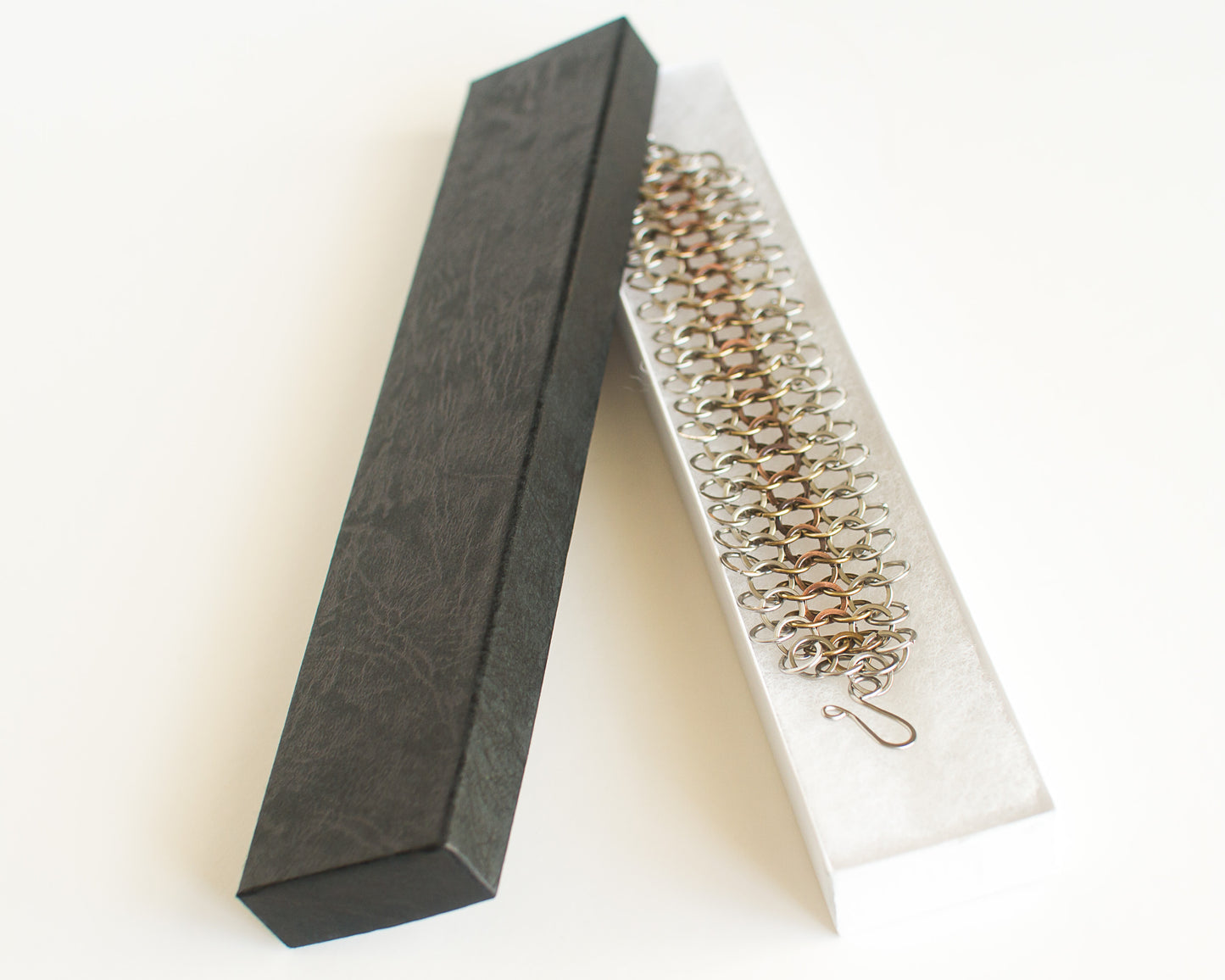 Copper brass and steel chainmaille bracelet in a black and white box on a light background