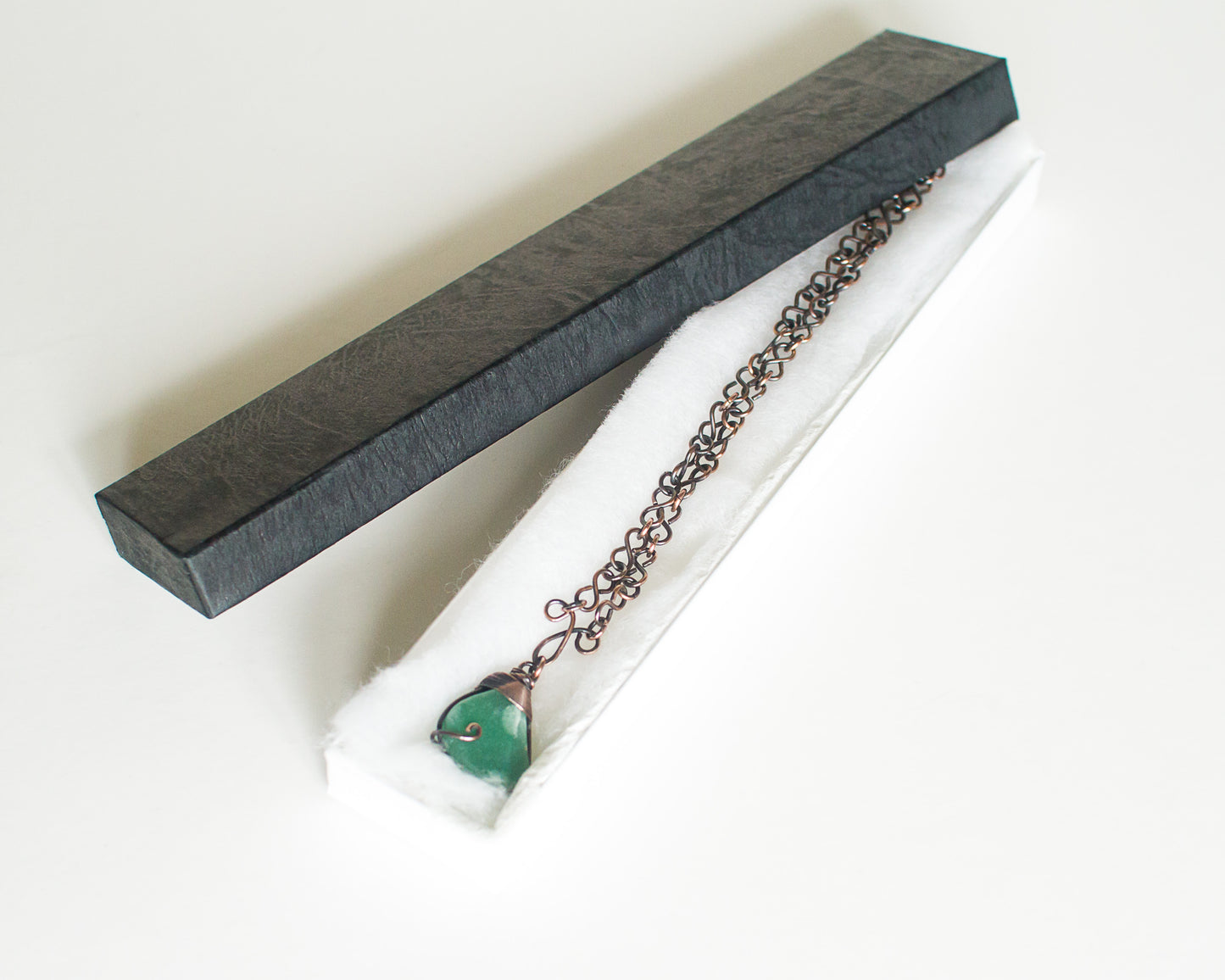 Copper necklace with a green stone pendant in a black presentation box on a white background