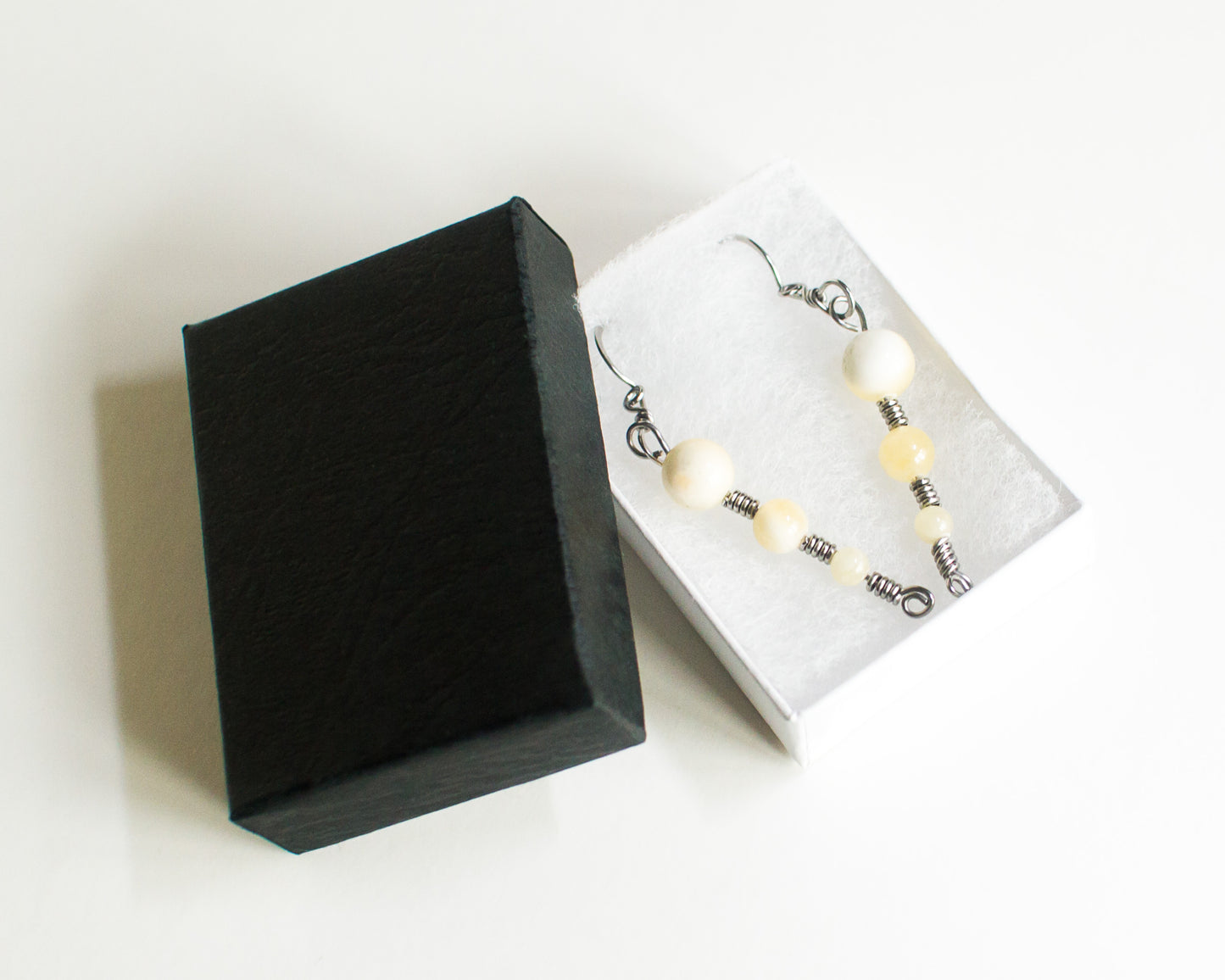 Black jewelry box with a white interior displaying a pair of earrings on a white background