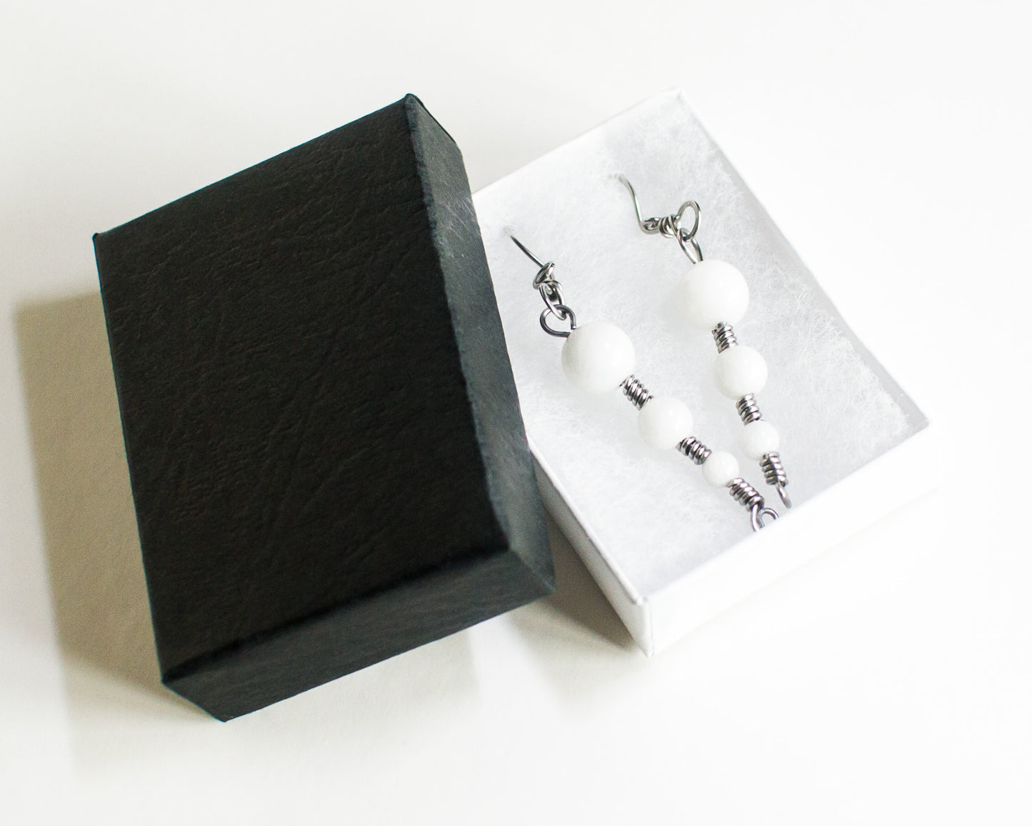 Black jewelry box with a white interior displaying earrings on a white background