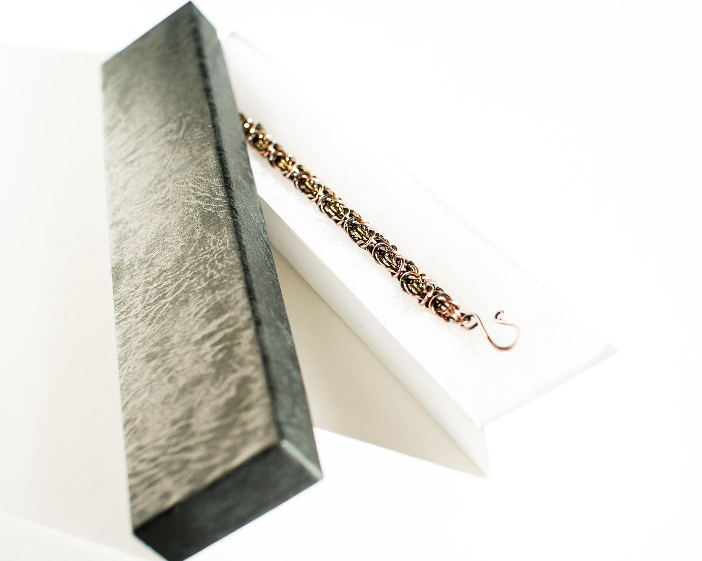 Copper and brass chain bracelet in a textured black box.