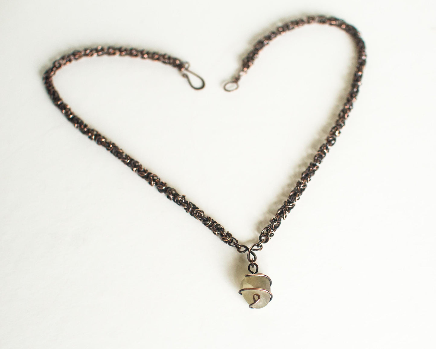 Copper Necklace forming a heart shape on a white background with a clear stone wire wrapped pendant at the bottom.