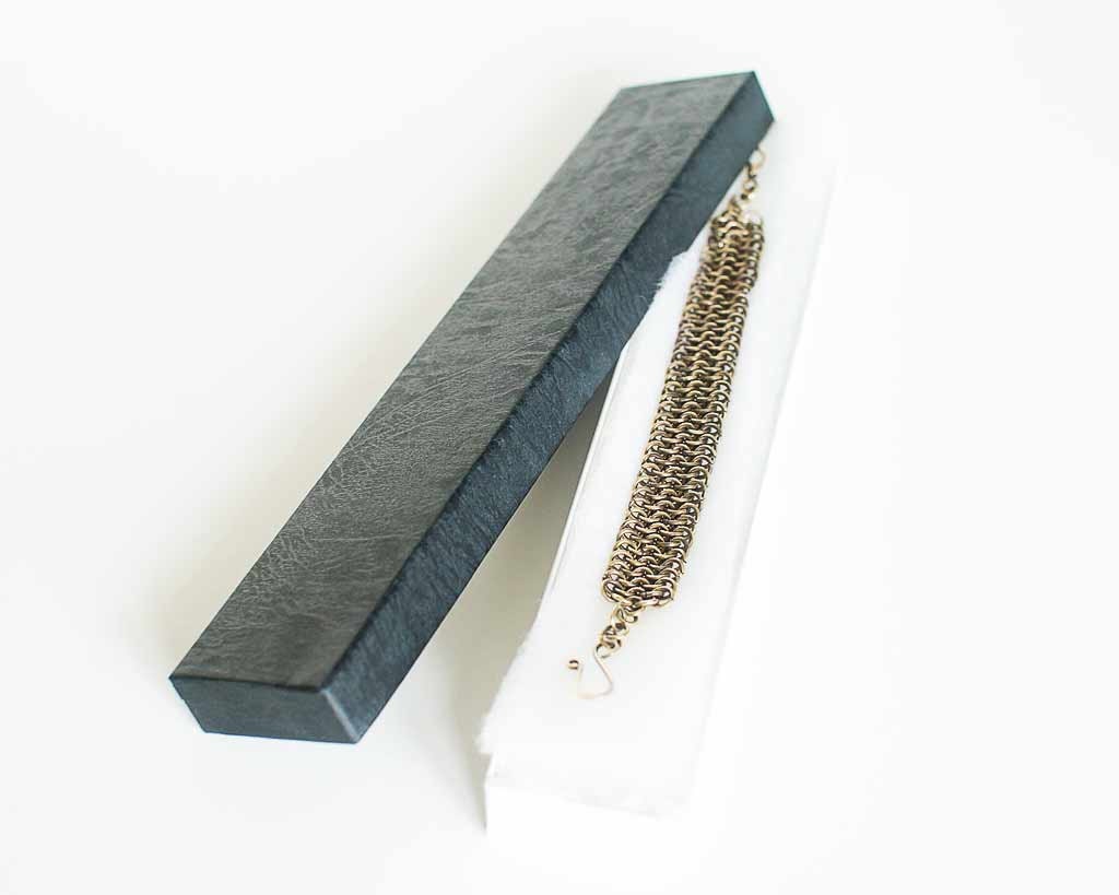 Brass chainmail bracelet in a black jewelry box on a white background.