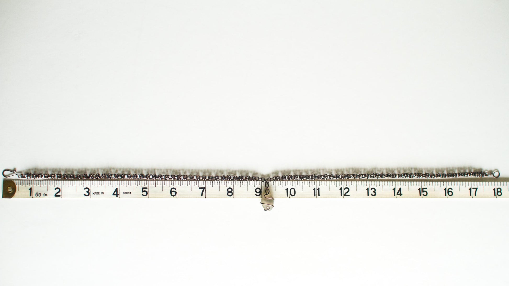 Copper necklace pictured against a tape measure showing a length of eighteen inches on a white background