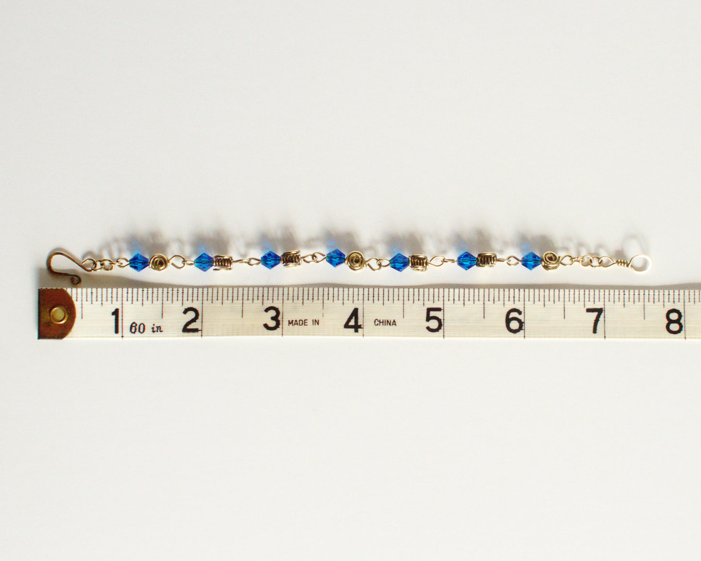 Bracelet with blue beads and gold accents on a measuring tape showing  alength of 7.5 inches or 19cm