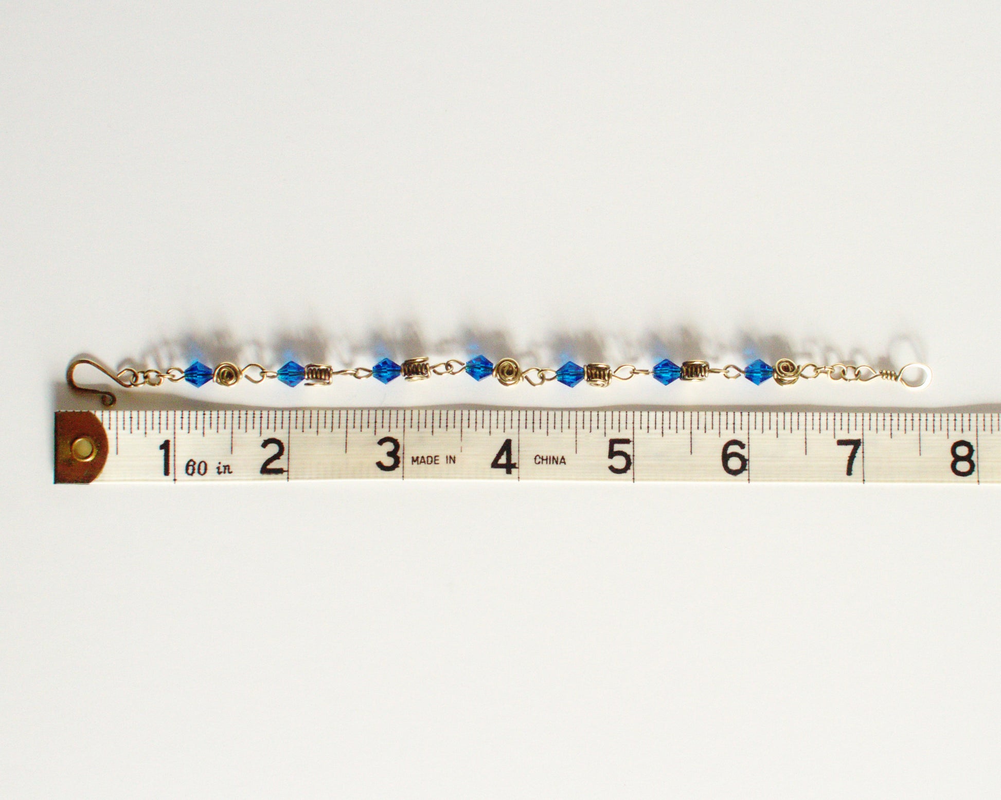 Bracelet with blue beads and gold accents on a measuring tape showing  alength of 7.5 inches or 19cm