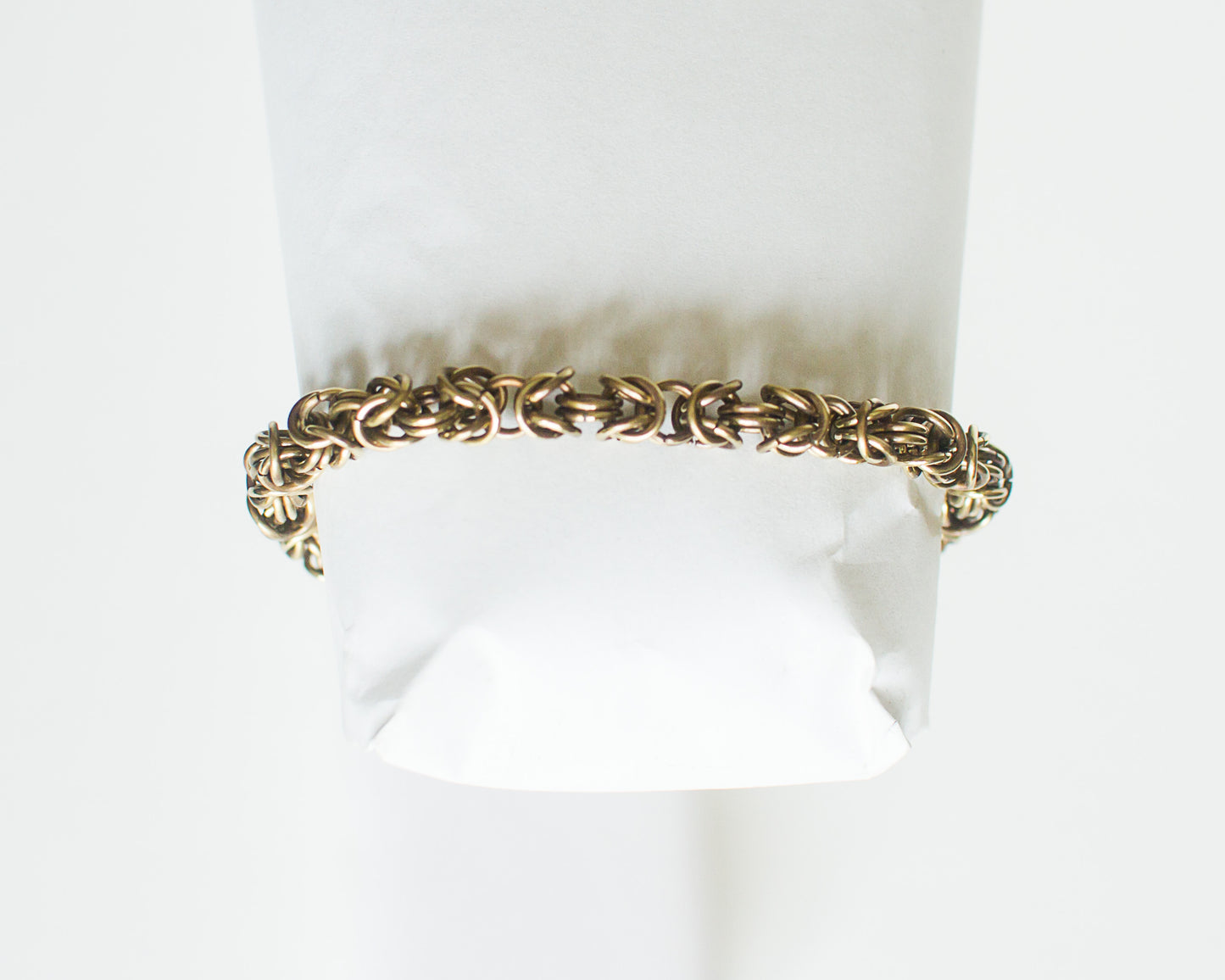 Brass chain bracelet on a white form on a white background.