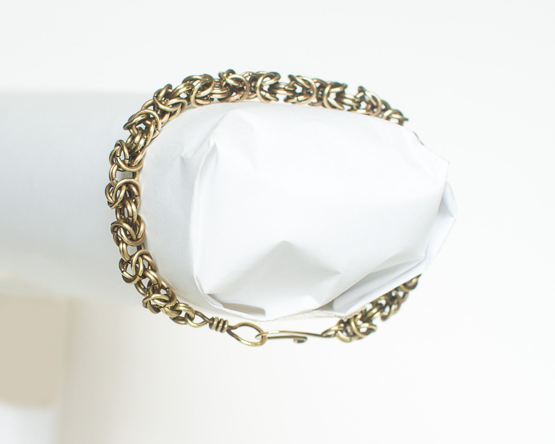 Brass chain bracelet on a white form on a white background.