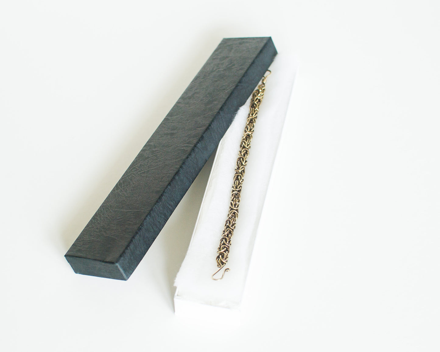 Brass chain bracelet on a white jewelley box with a black lid.