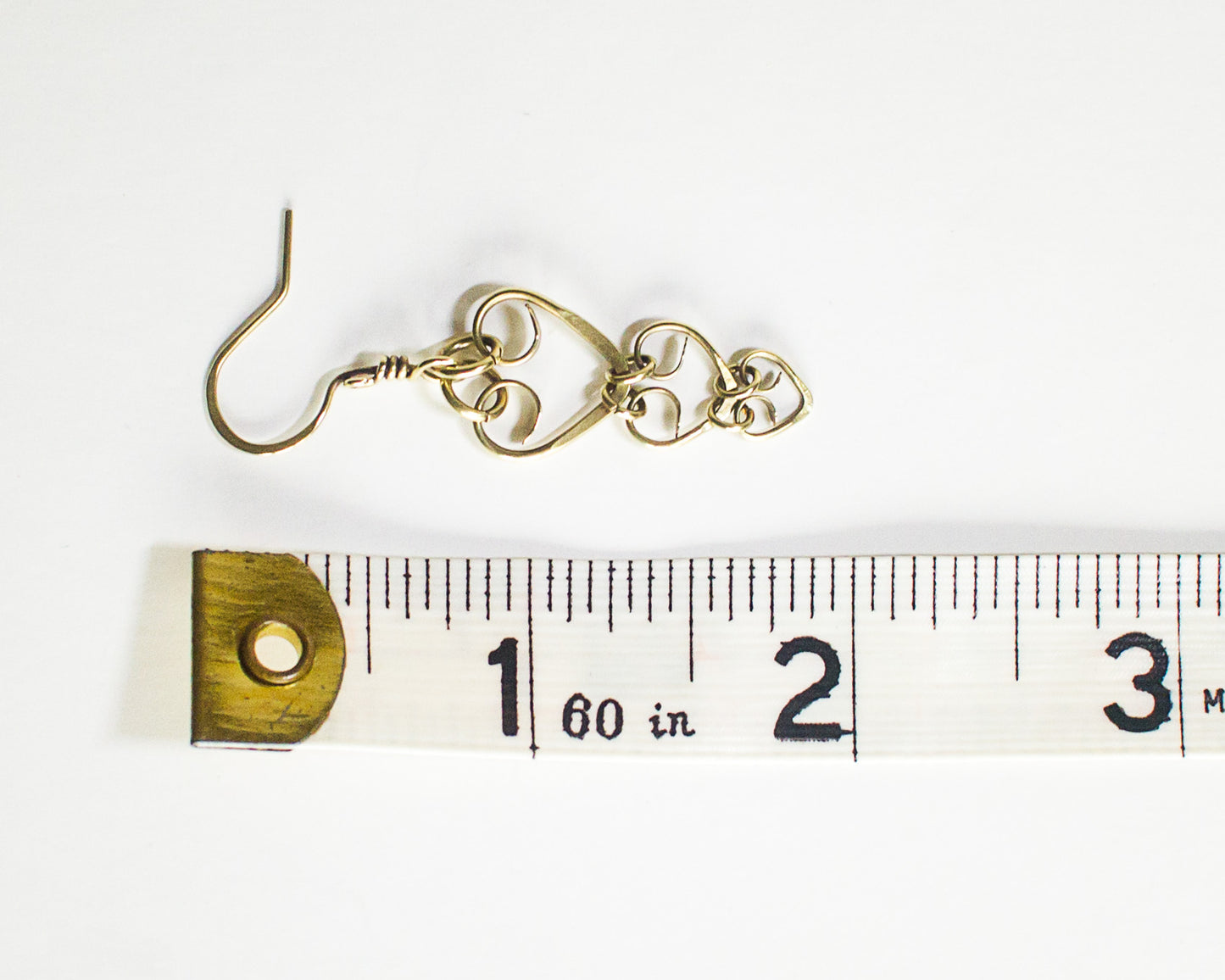 Brass earring on a ruler for scale on a white background - ruler shows a length of 1 7/8 inches or 4.7cm long