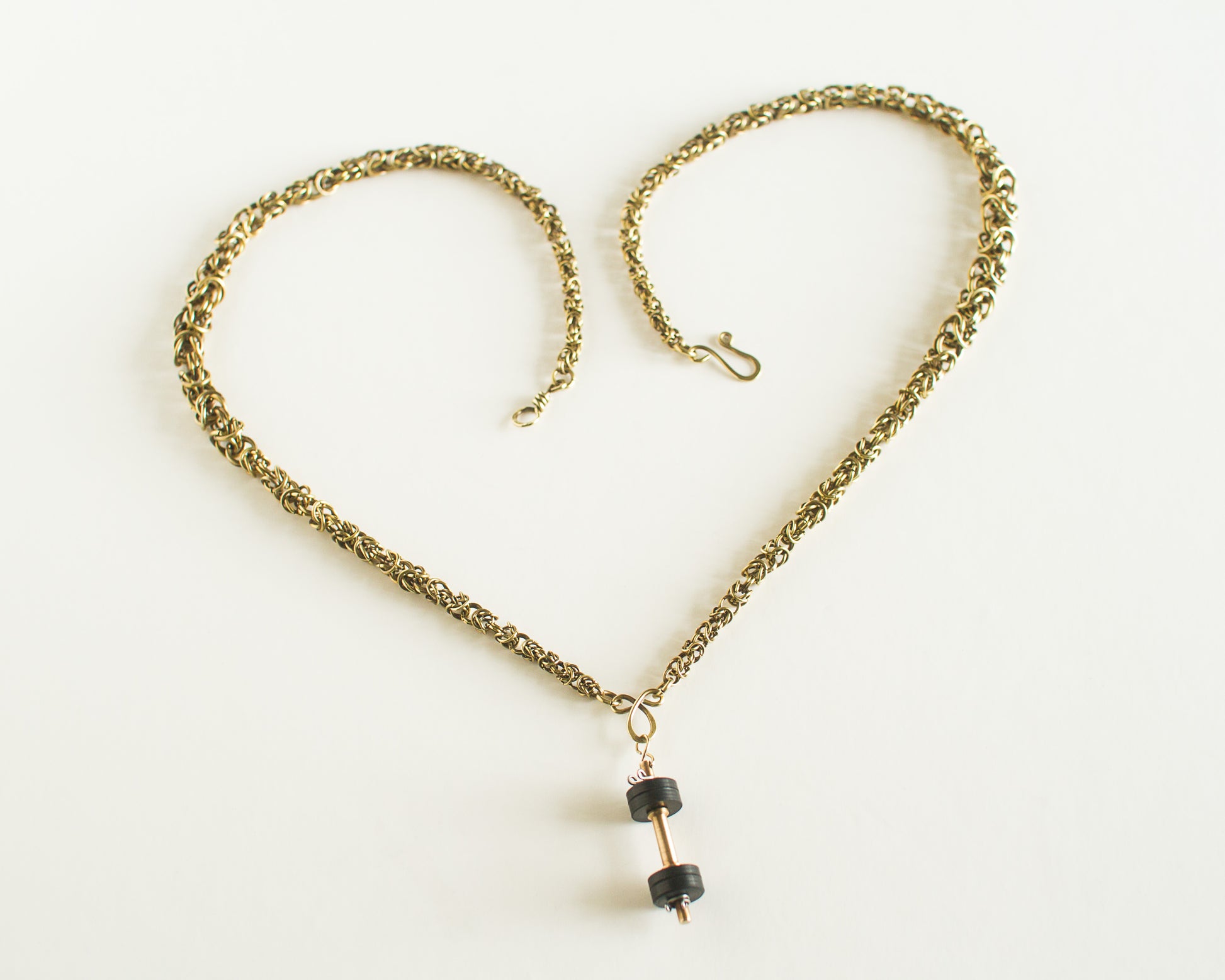 Gold chain necklace with a dumbell pendant on a white background