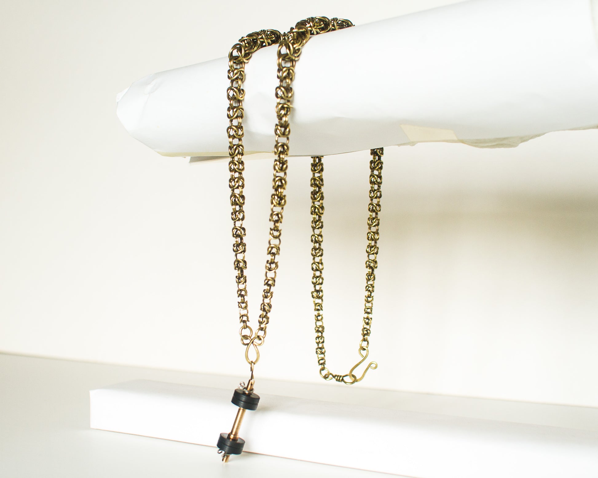 Gold chain necklace with dumbell pendant draped over a white surface