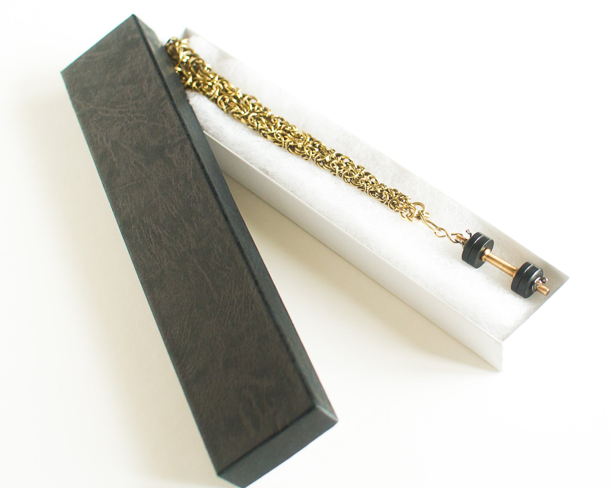 Gold chain with dumbell pendant in a black box on a white background