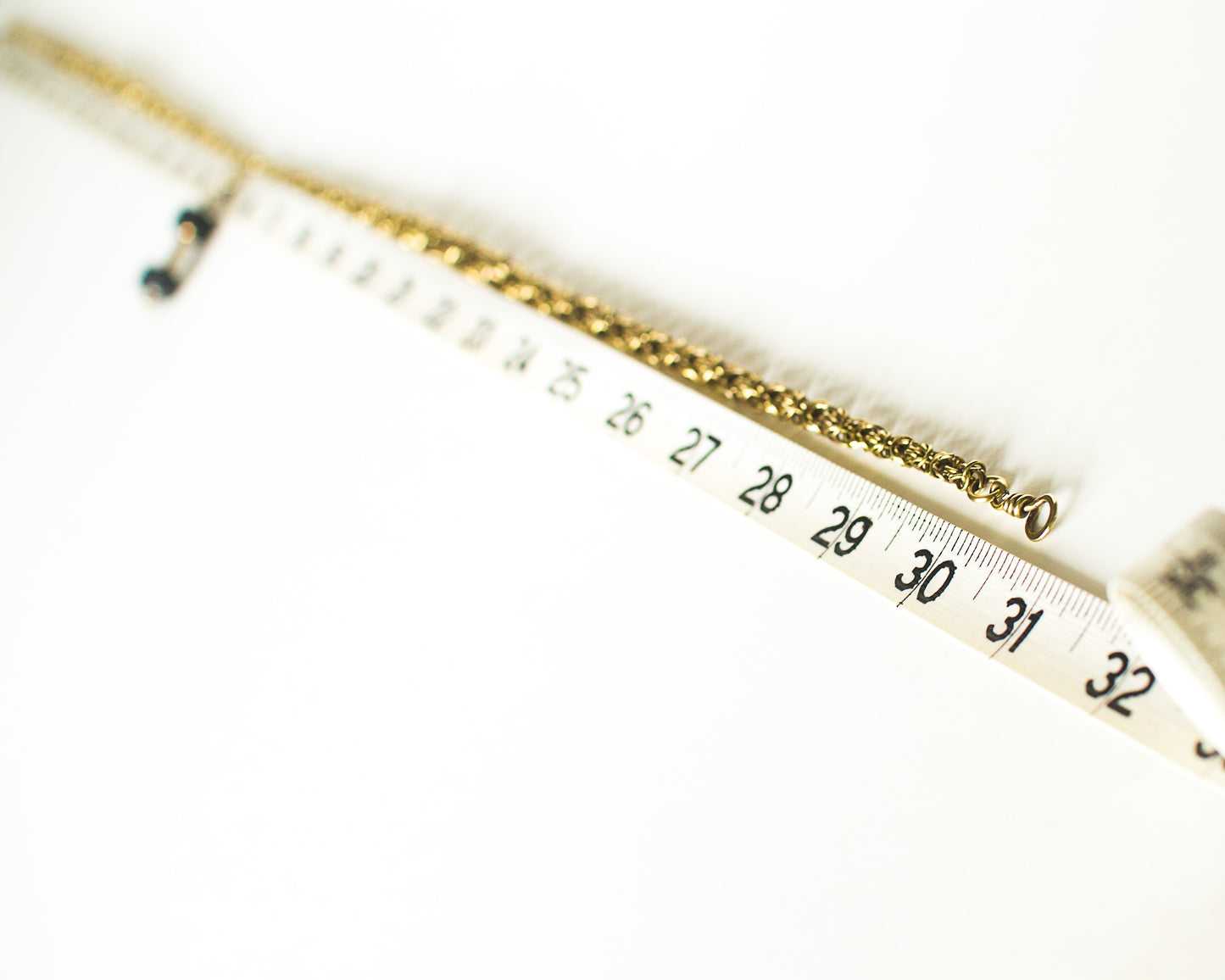 Gold necklace with a chain on a white background with tape measure showing a length of thirty and three quarter inches
