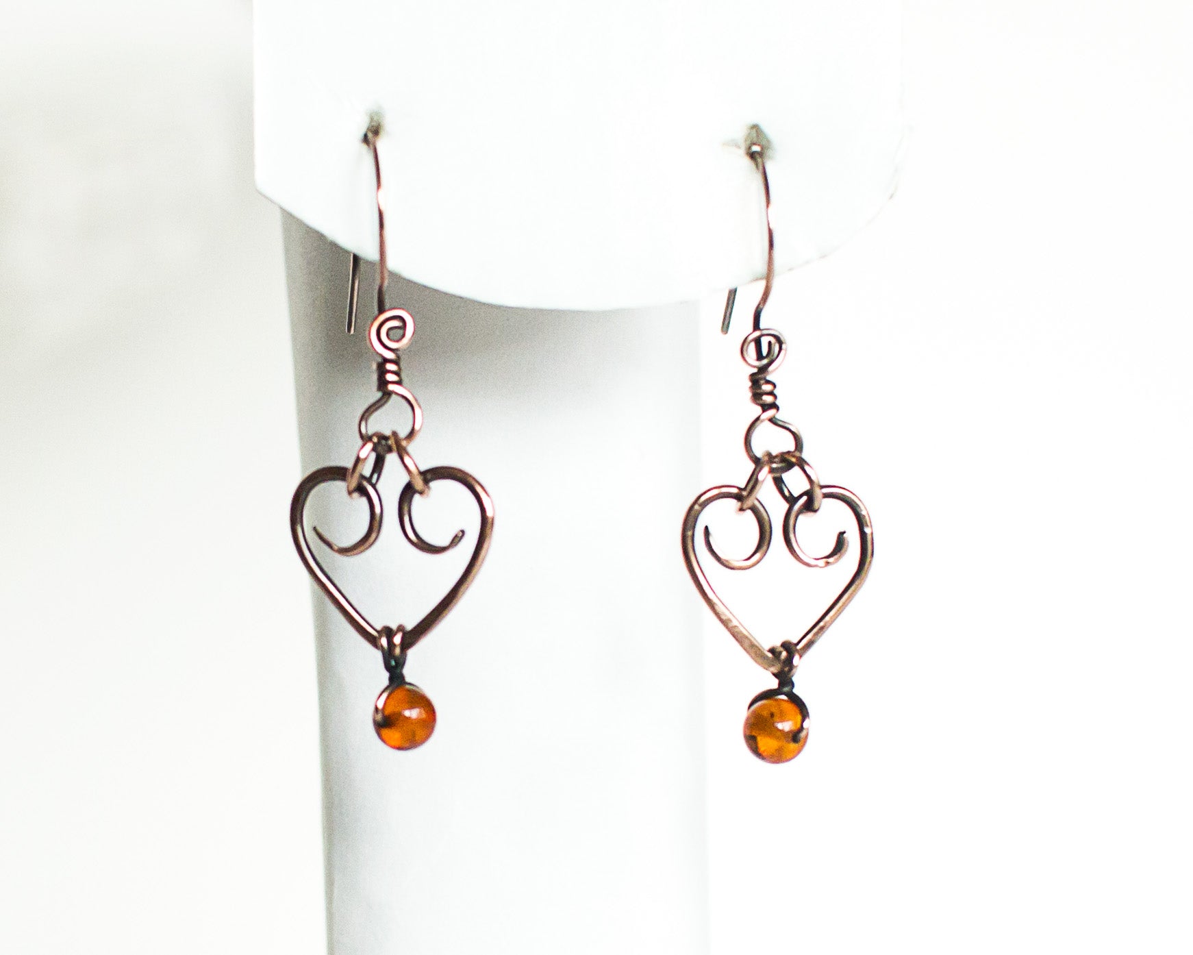 Heart-shaped copper earrings with amber beads on a white stand.