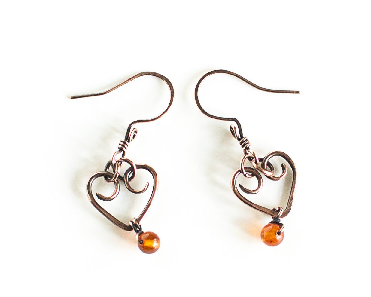 Heart-shaped copper earrings with amber beads on a white background