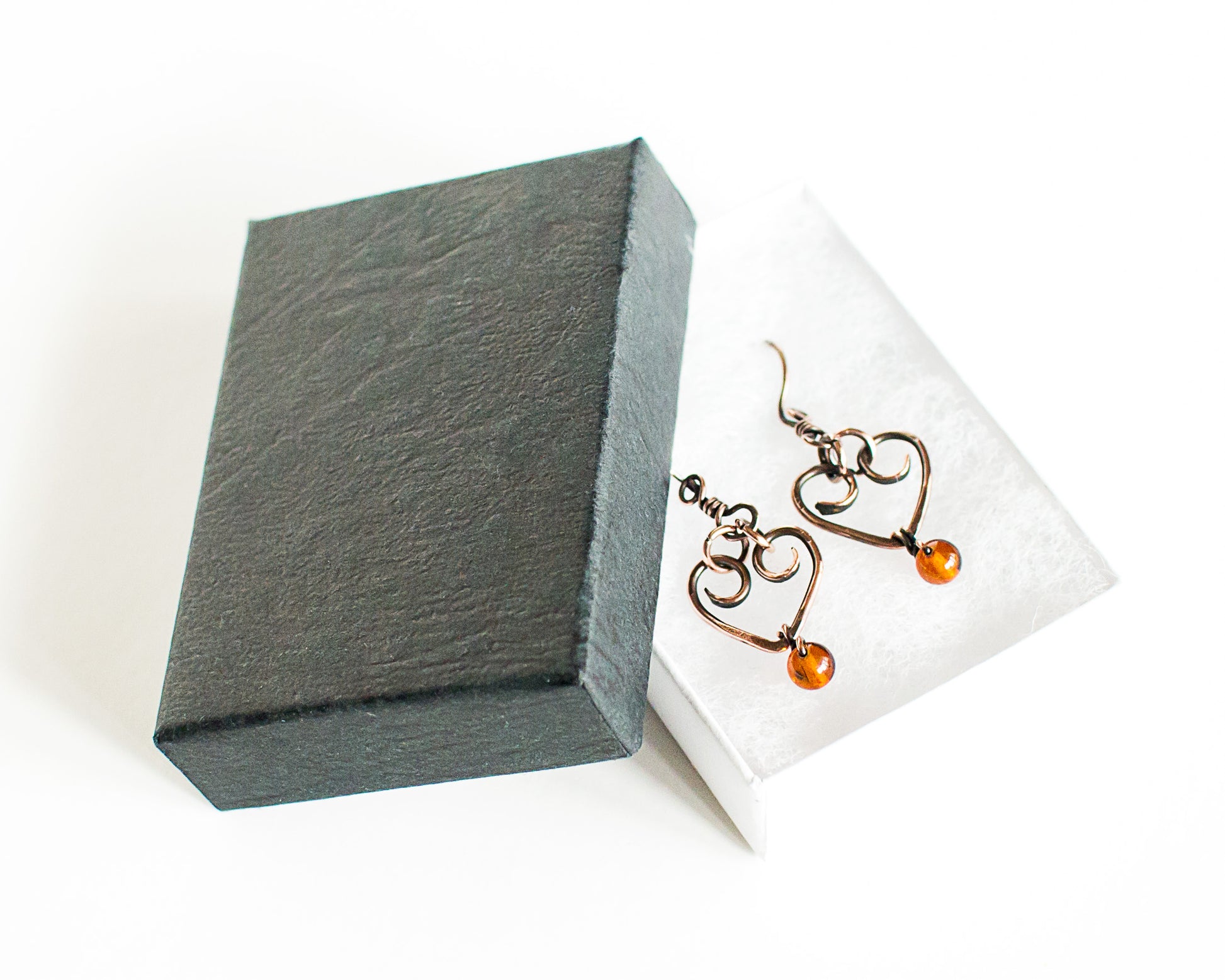 Heart-shaped copper earrings with amber beads in a black jewelry box on a white background