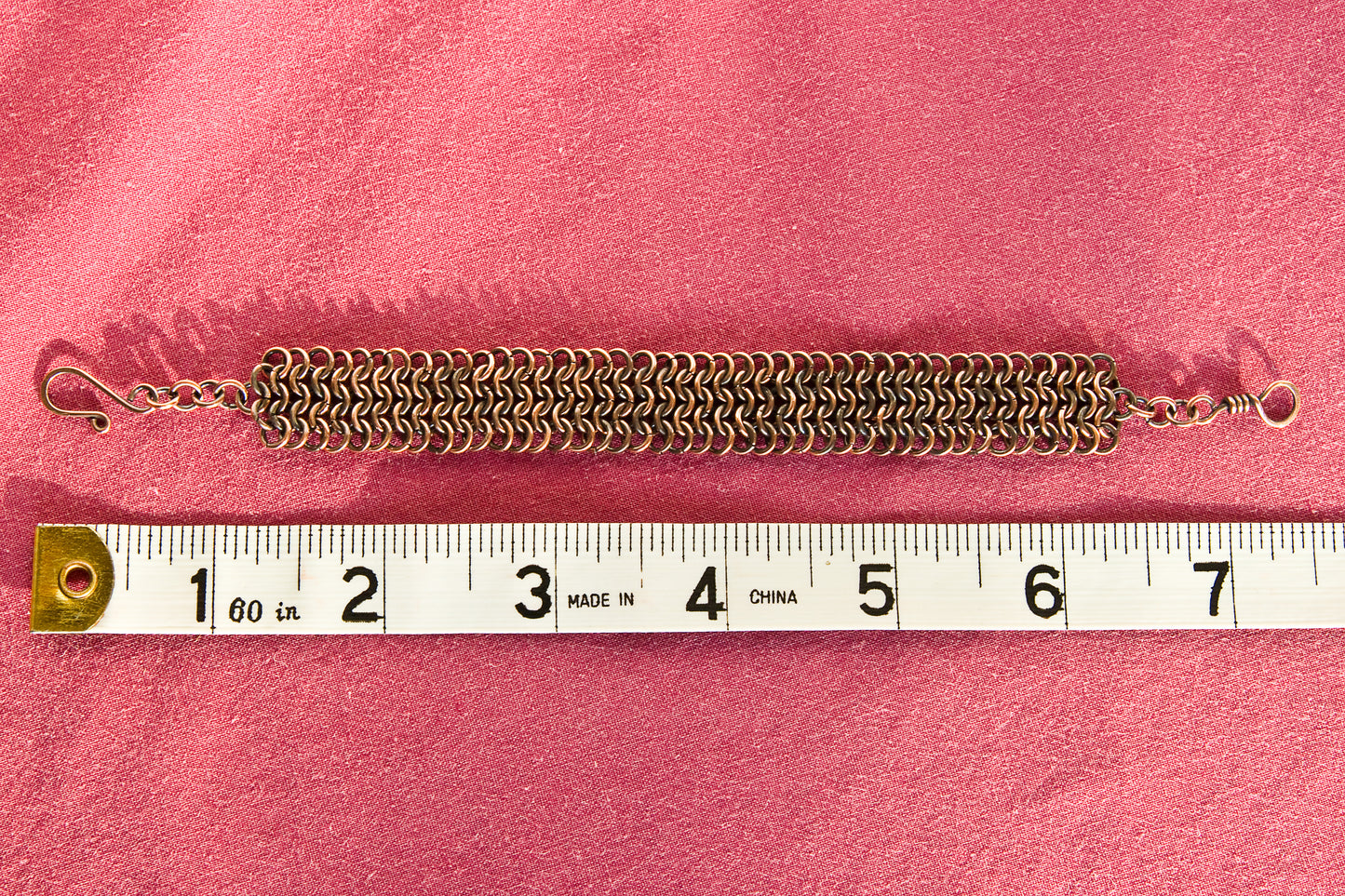 Copper chain bracelet on a red surface with a ruler for scale - showing a length of 7.5 inches or 19cm.