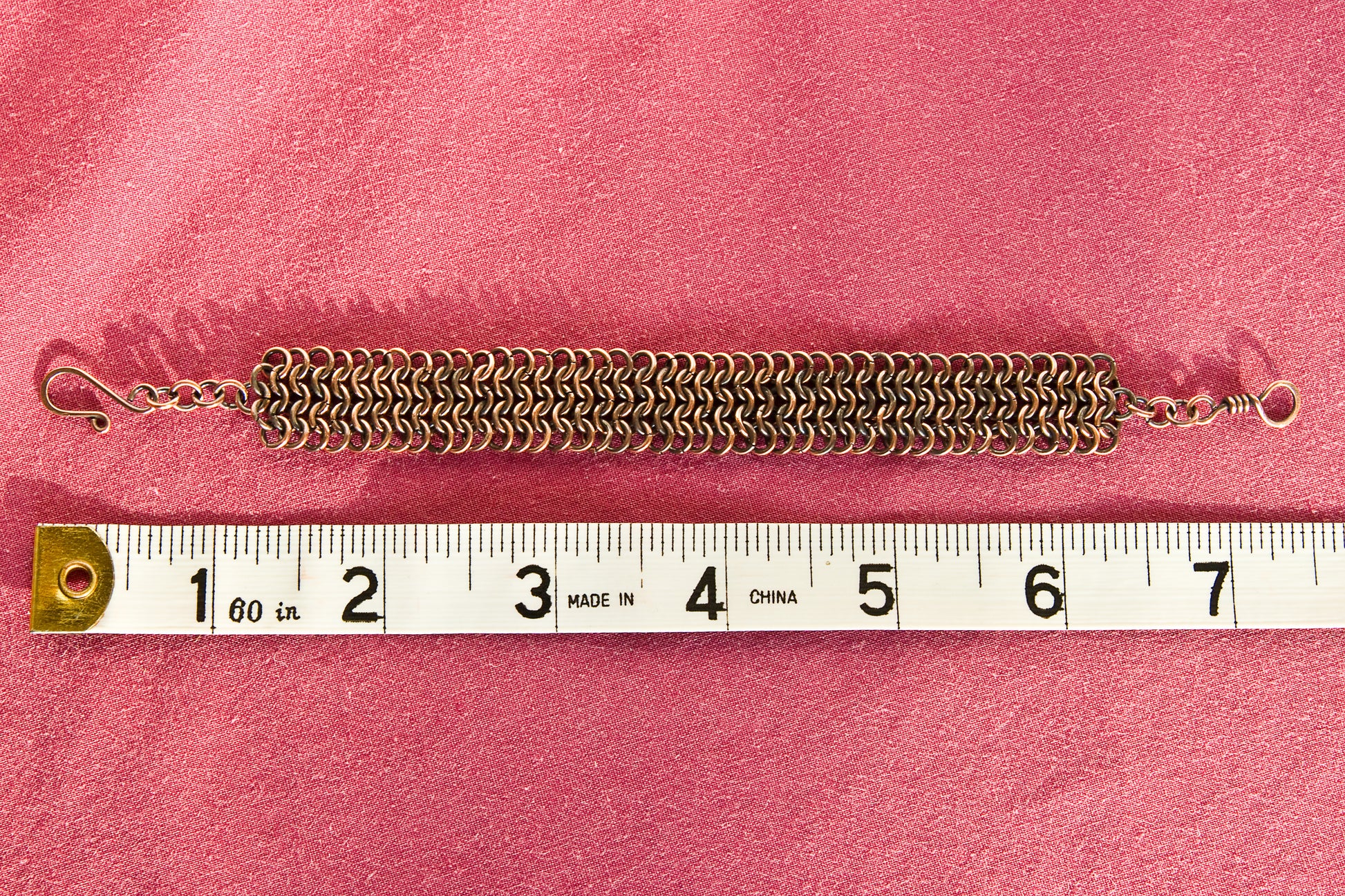 Copper chain bracelet on a red surface with a ruler for scale - showing a length of 7.5 inches or 19cm.