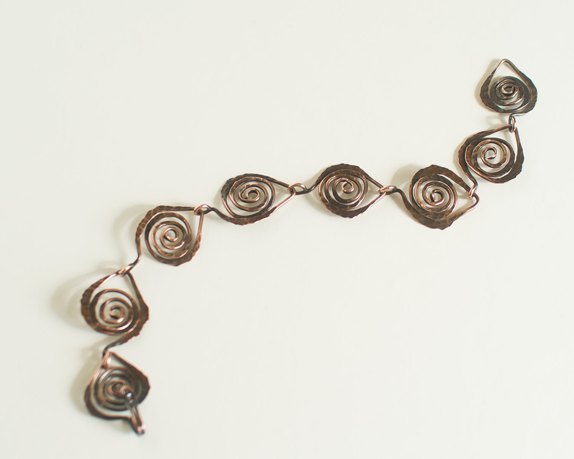 Copper spiral bracelet with leaf shaped links on a white background