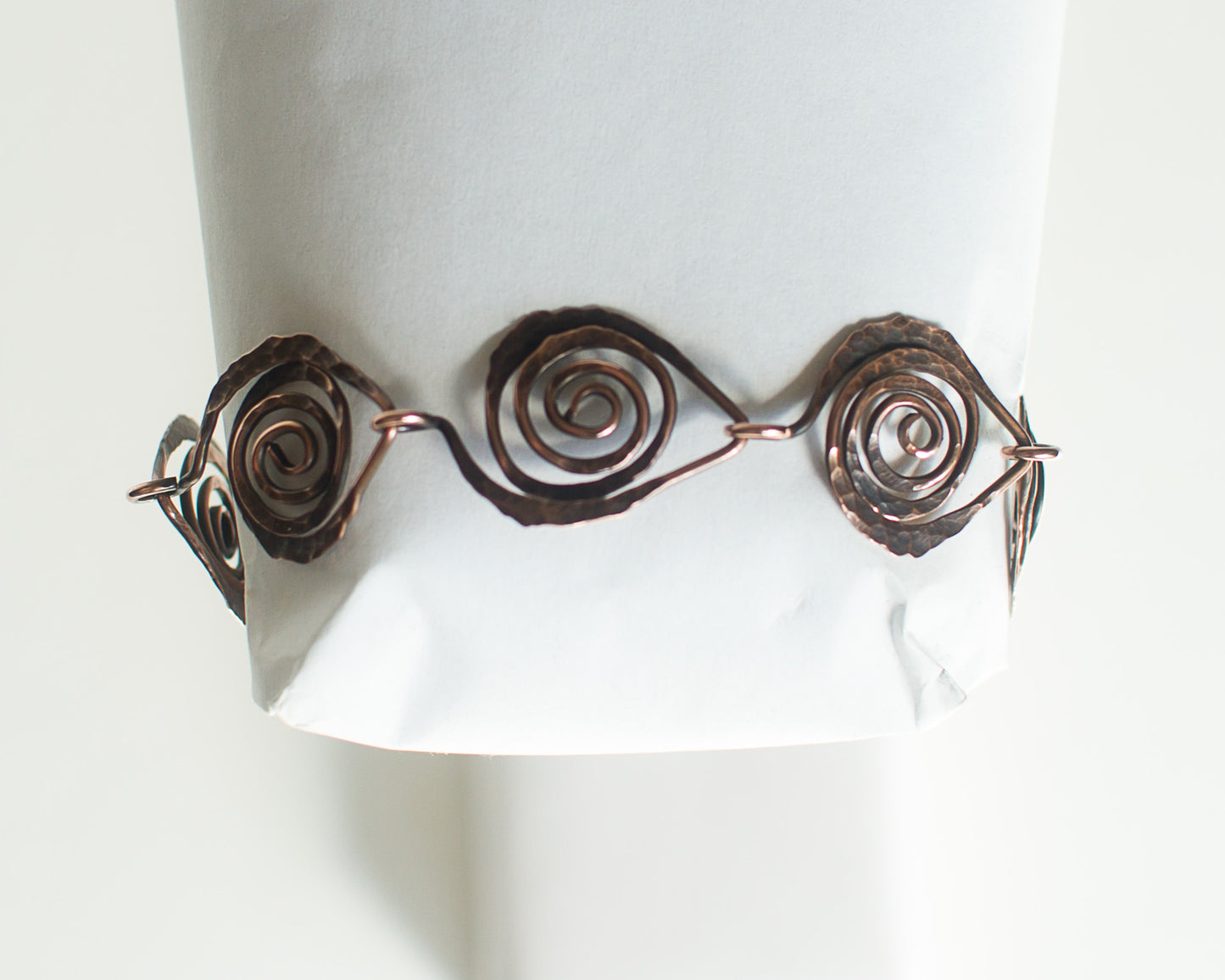 Copper bracelet with spiral design leaf shapes on a white background