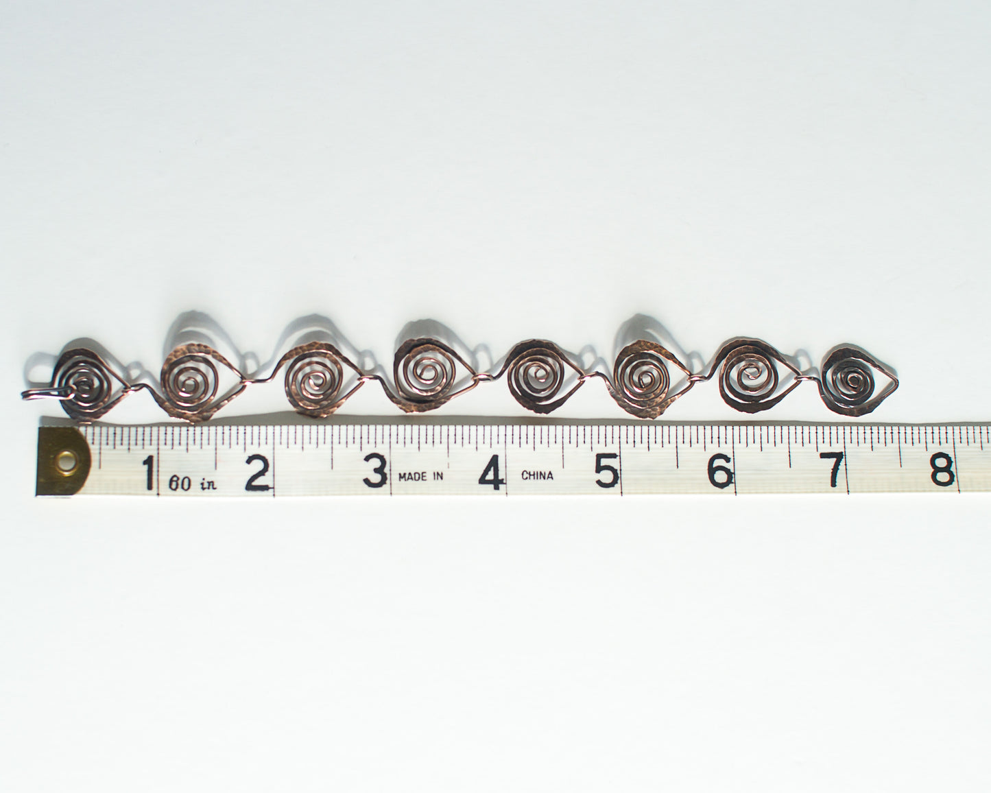 Copper bracelet with spiral design on a white background, measured against a ruler - showing a length of 7.5 inches or 19cm.