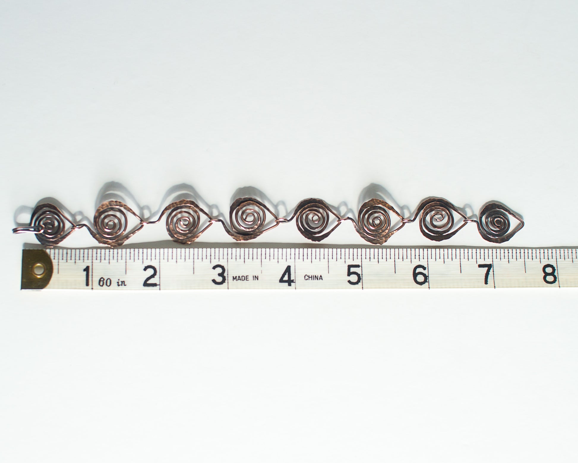 Copper bracelet with spiral design on a white background, measured against a ruler - showing a length of 7.5 inches or 19cm.