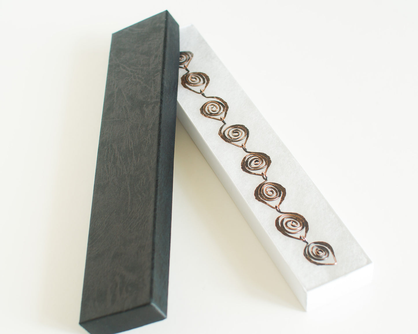 Copper bracelet with spiral leaf links shown inside a Black and white box on a white background