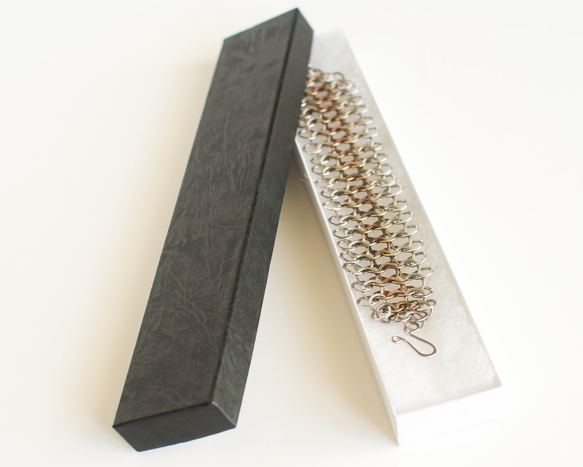 Copper brass and steel chainmaille bracelet in a black and white box on a light background