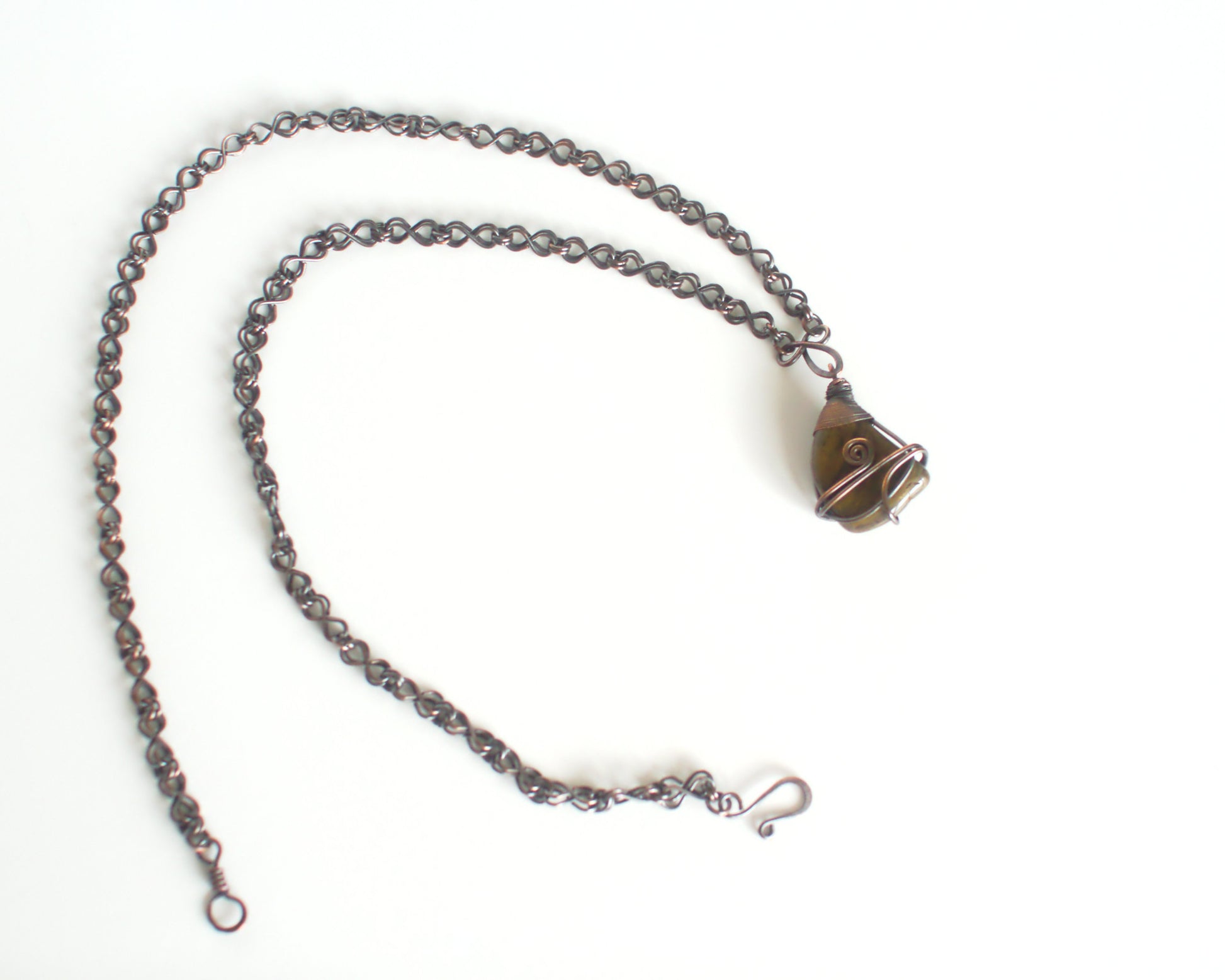 Copper chain necklace with a wire wrapped green stone pendant on a white background