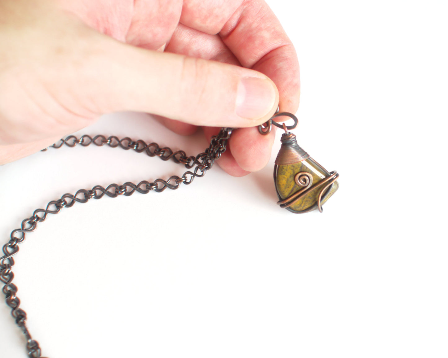 Hand holding a necklace with a detailed pendant against a white background