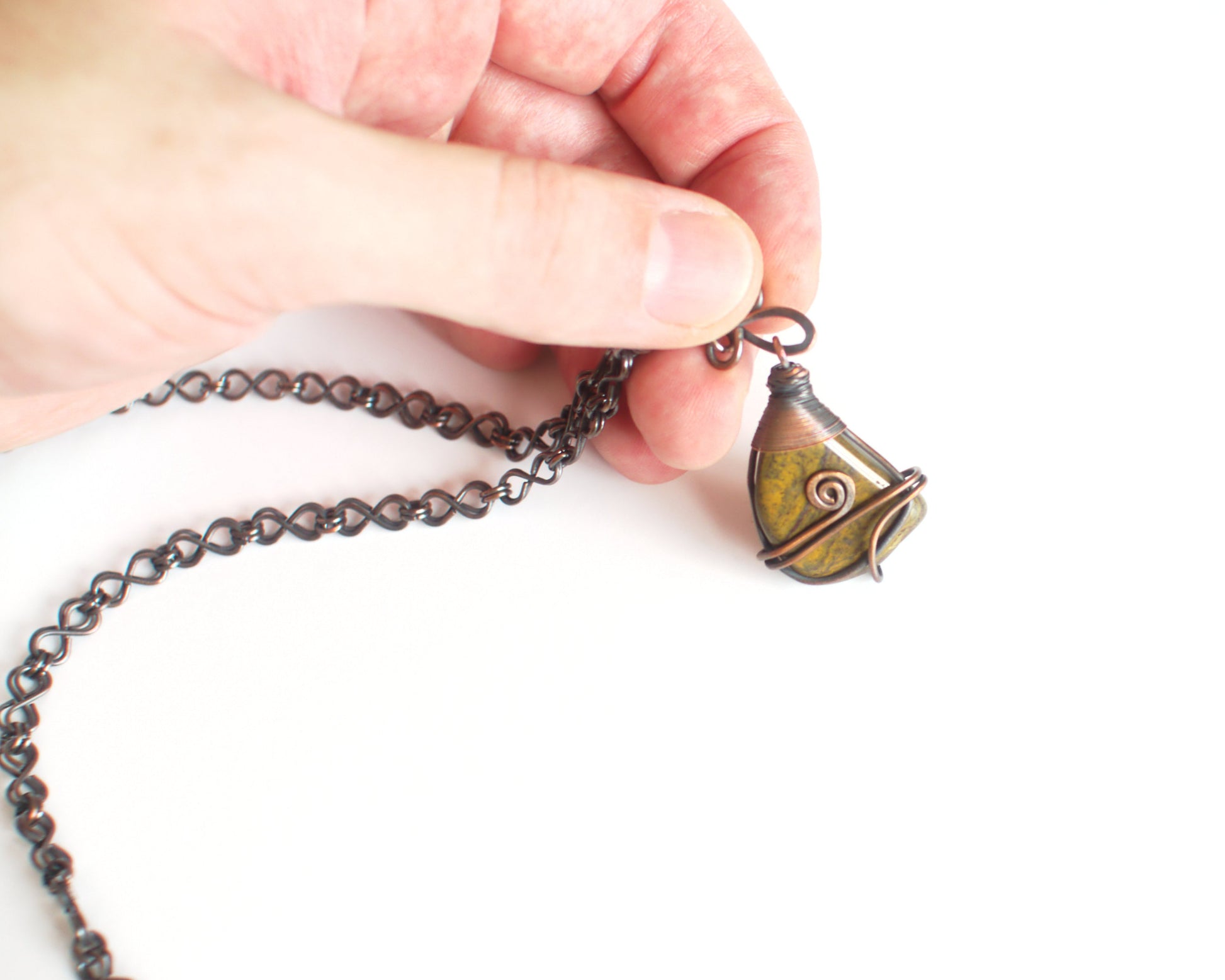 Hand holding a necklace with a detailed pendant against a white background
