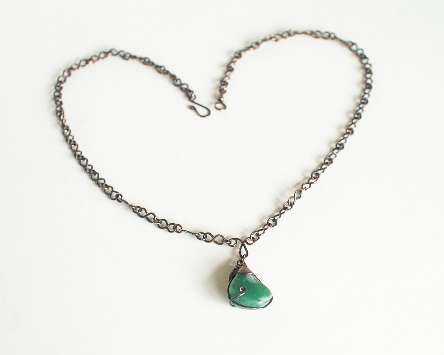 Copper necklace with a green pendant on a white background, neckalce chain has infinity shaped links and the green stone is wire wrapped.