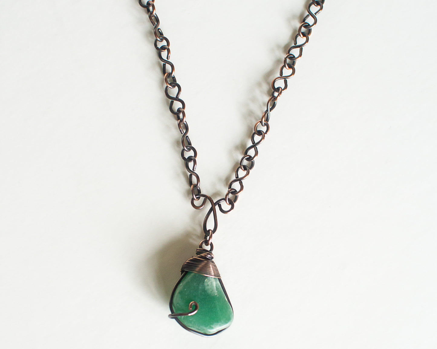 Necklace with a wire wrapped green stone pendant on an oxidized copper chain against a white background.