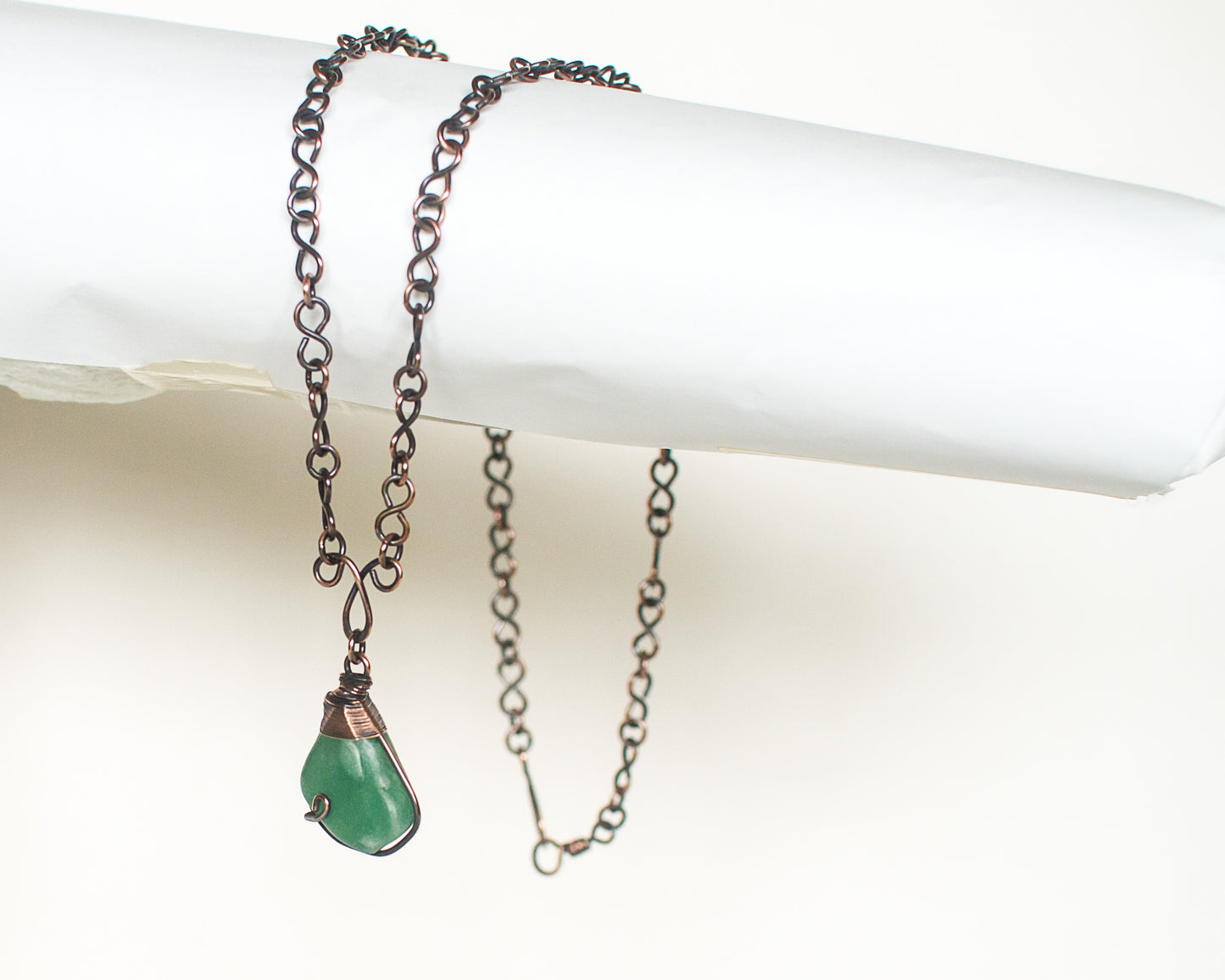 Copper chain necklace with a green stone pendant on a white surface