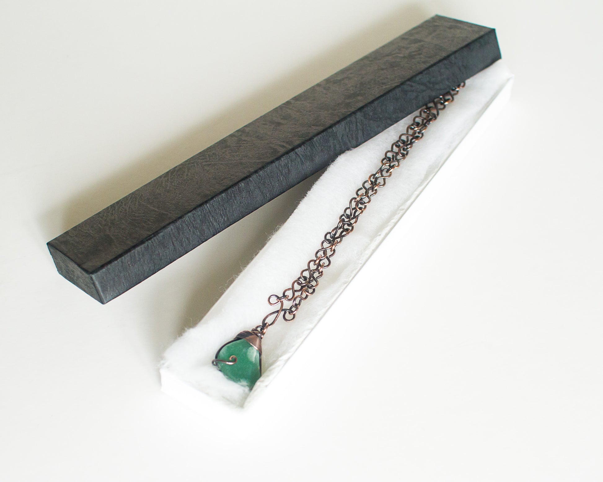 Copper necklace with a green stone pendant in a black presentation box on a white background
