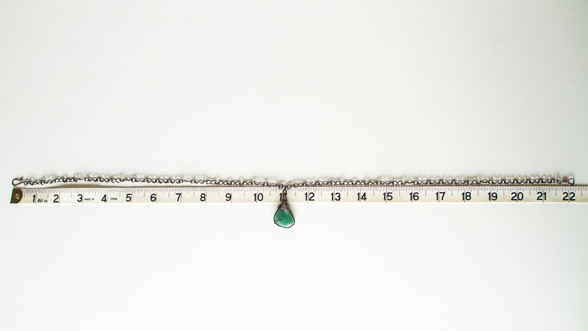 Green stone pendant on a copper chain against a white background with a measuring tape for scale - showing 22" length for the chain.