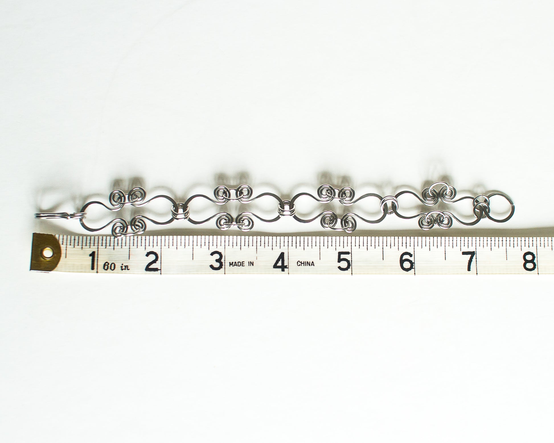 Silver bracelet on a white background with a ruler for scale - showing a length just over 7.5 inches or 19cm.