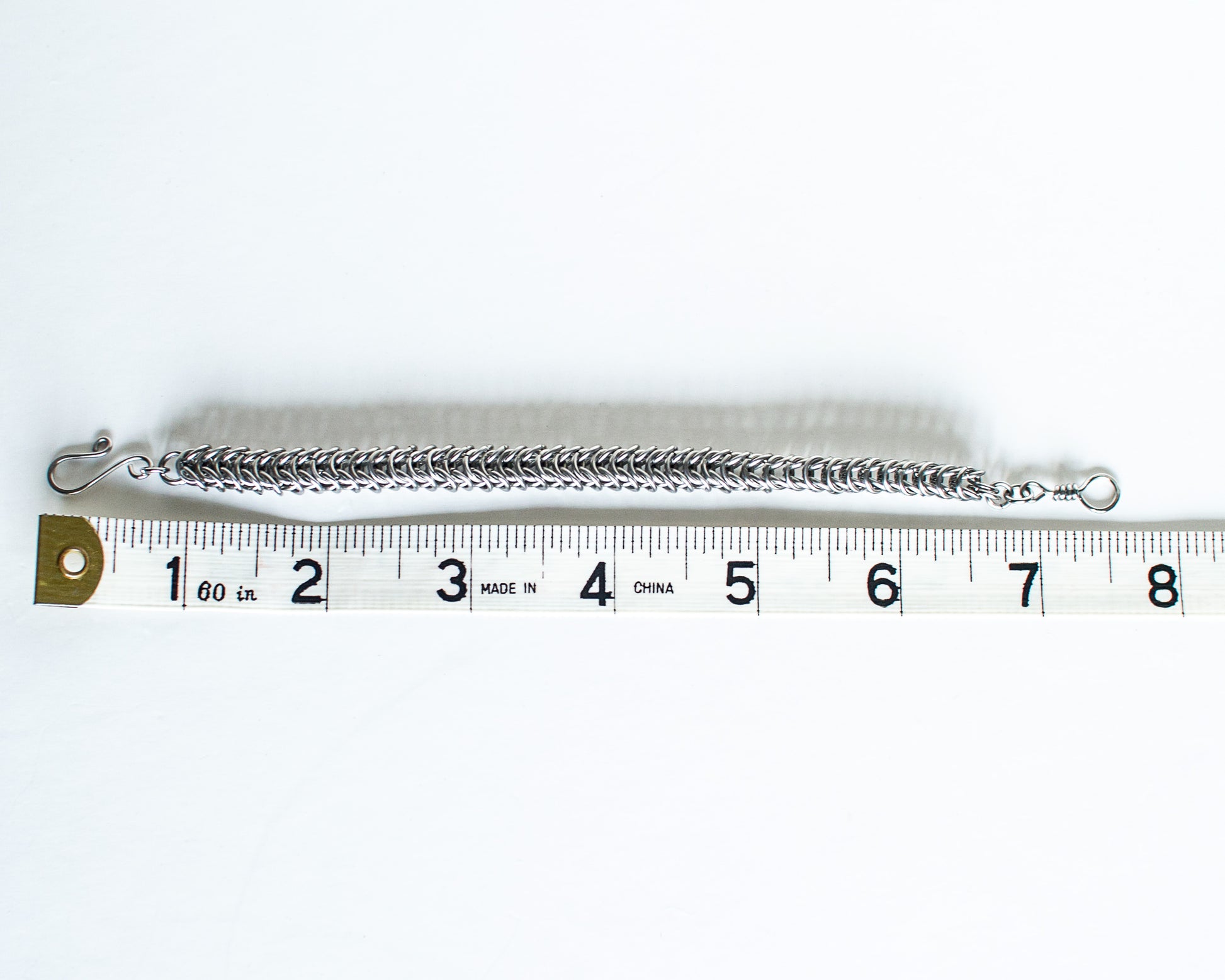 Steel chain bracelet on a white background with a ruler for scale - showing a length of 7.5 inches or 9cm long.