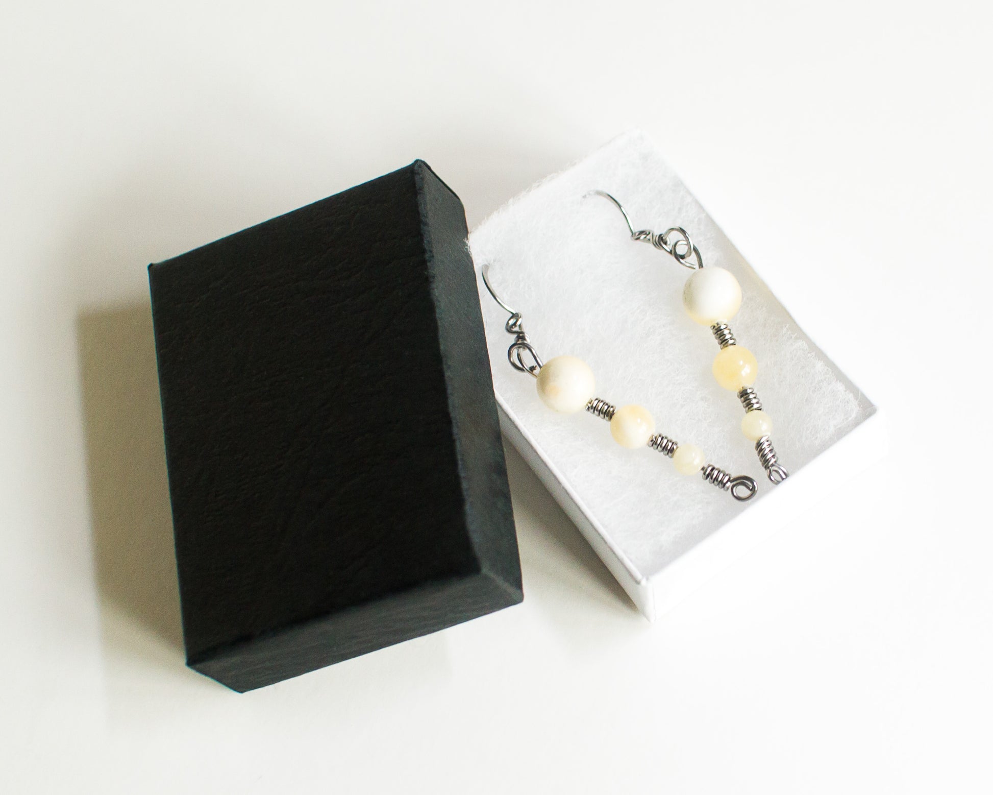 Black jewelry box with a white interior displaying a pair of earrings on a white background