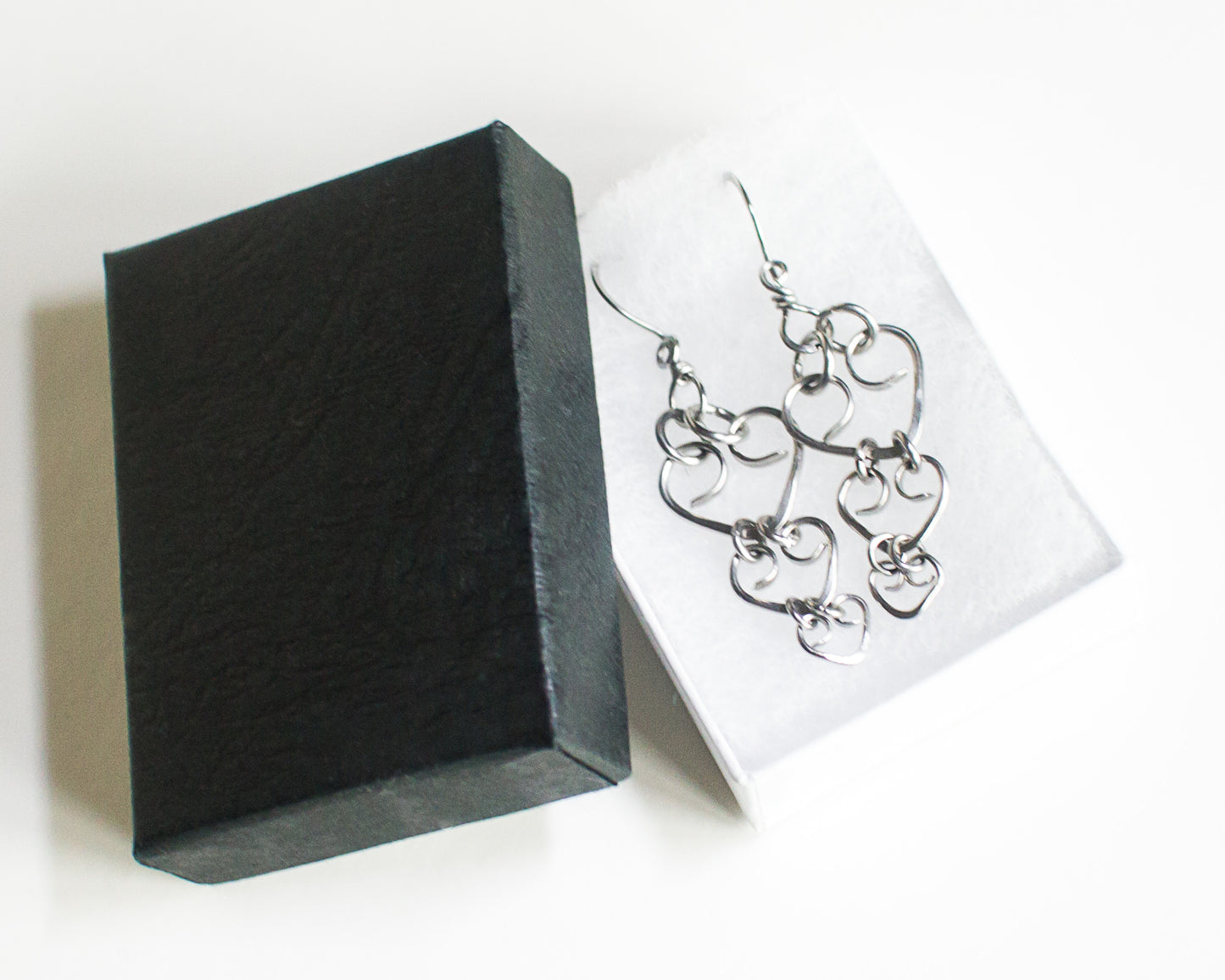 Steel heart-shaped earrings on a white card with a black jewelry box.