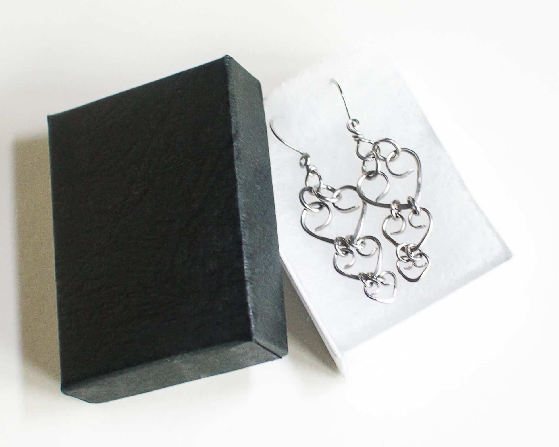 Steel heart-shaped earrings on a white card with a black jewelry box.