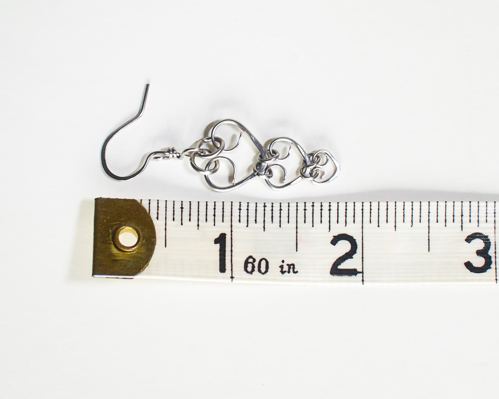 Steel heart-shaped earrings on a ruler for size reference - showing a length of 1.75 inches or 4.3cm long.