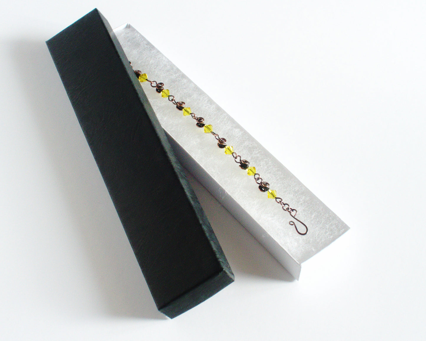 Copper Bracelet with yellow beads in a black jewellery box  on a white background.