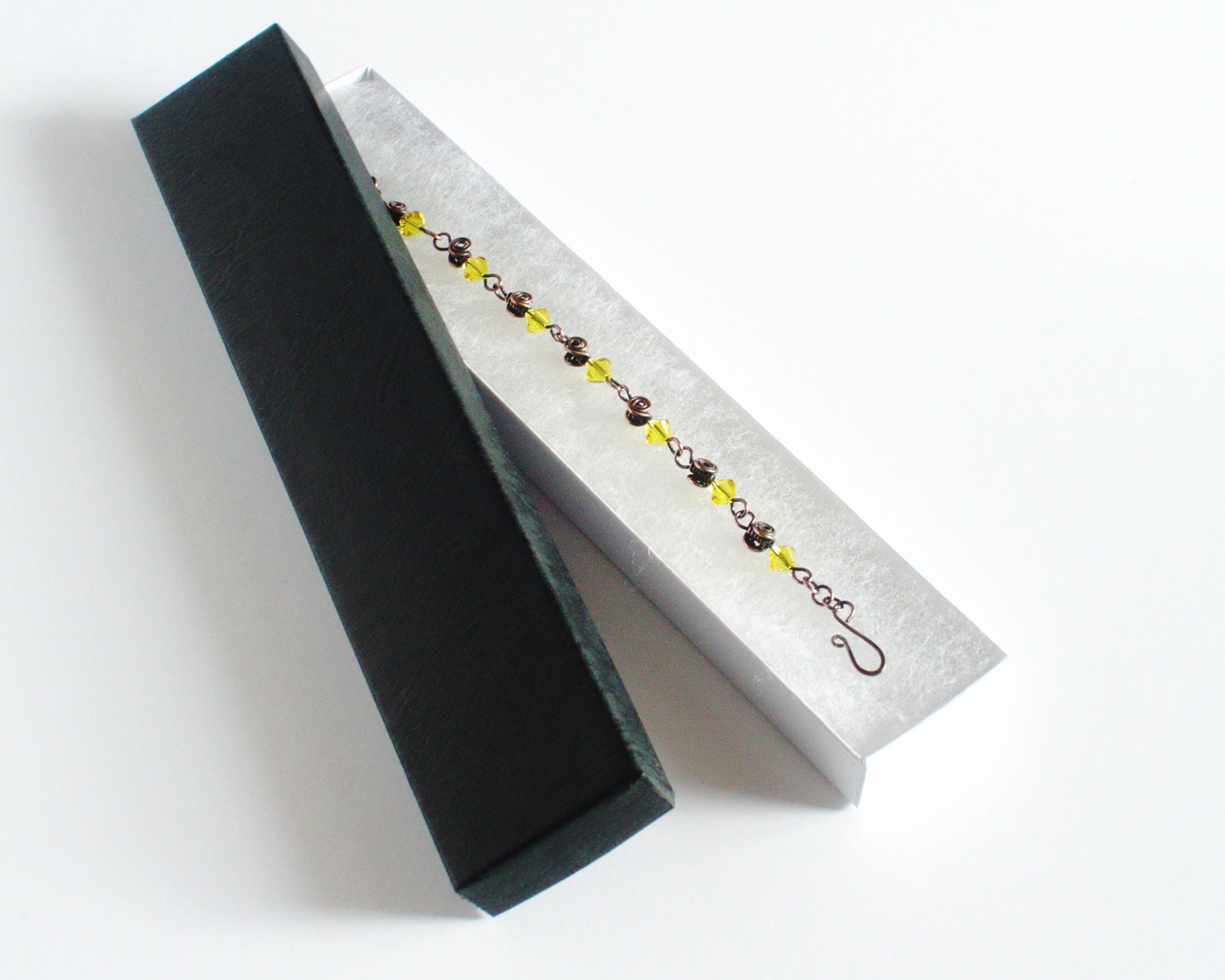 Copper Bracelet with yellow beads in a black jewellery box  on a white background.