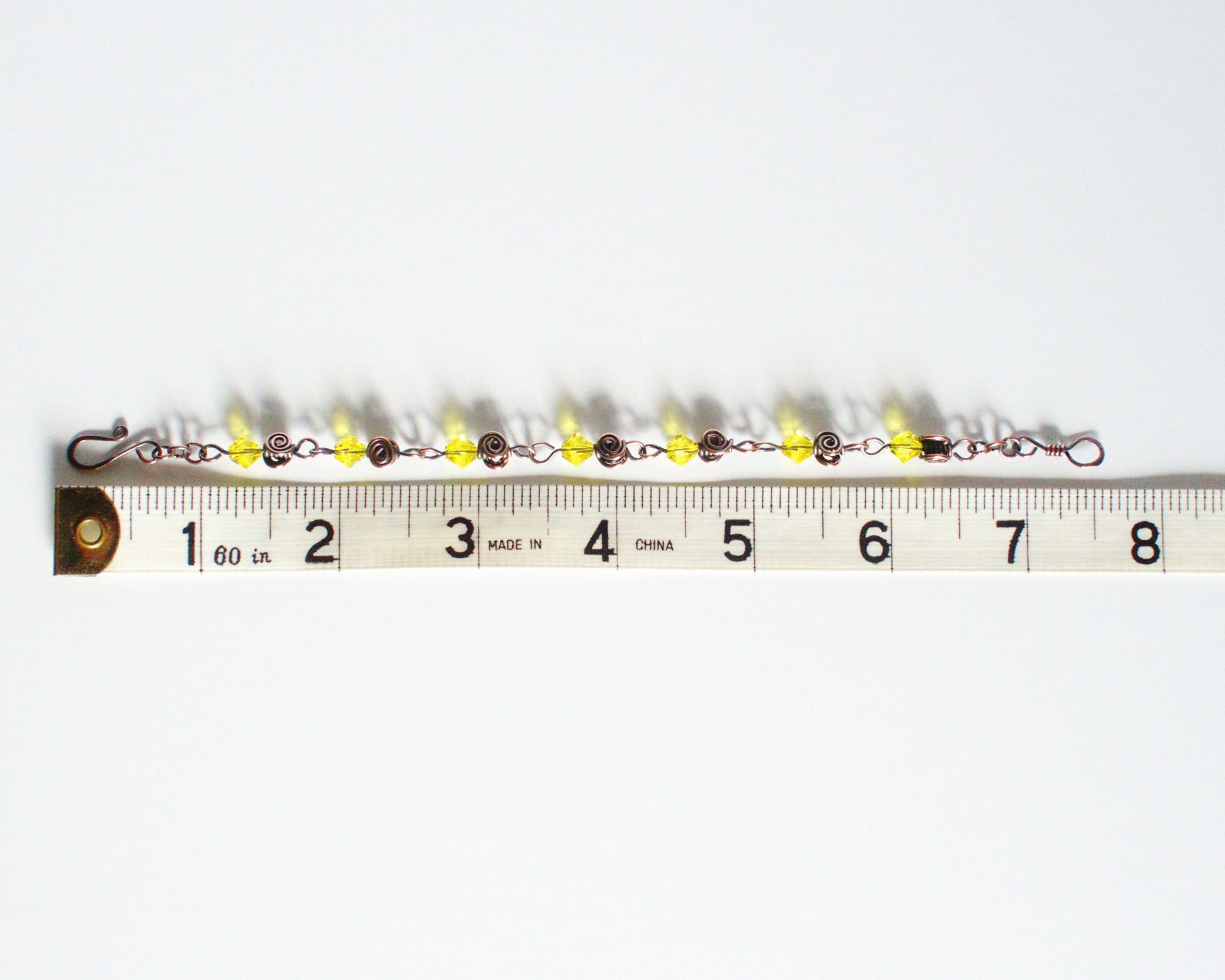 Bracelet with yellow beads on a white background, measured against a tape measure showing a length of 7.5 inches or 19cm.