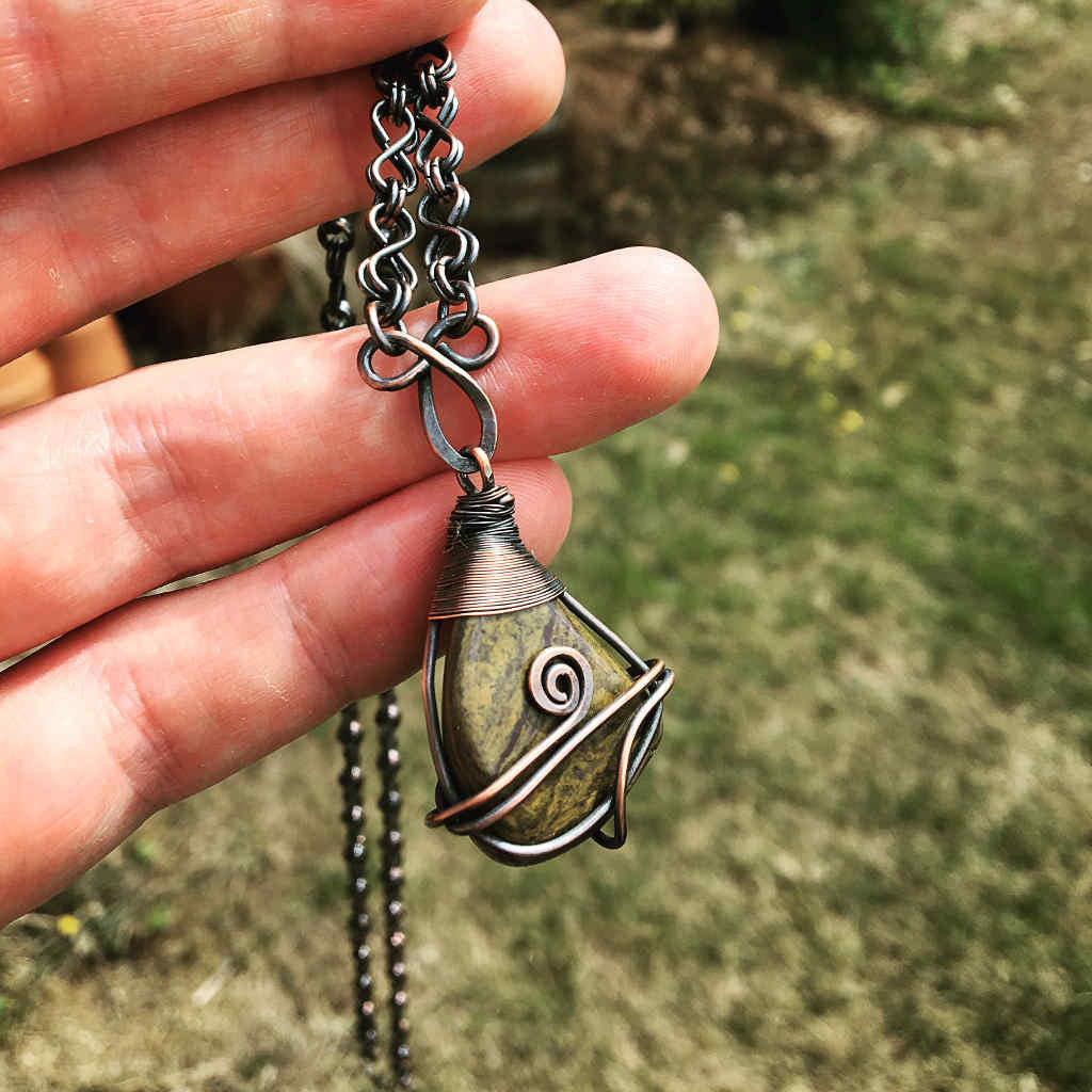 Hand holding a necklace with a decorative pendant against a blurred natural background