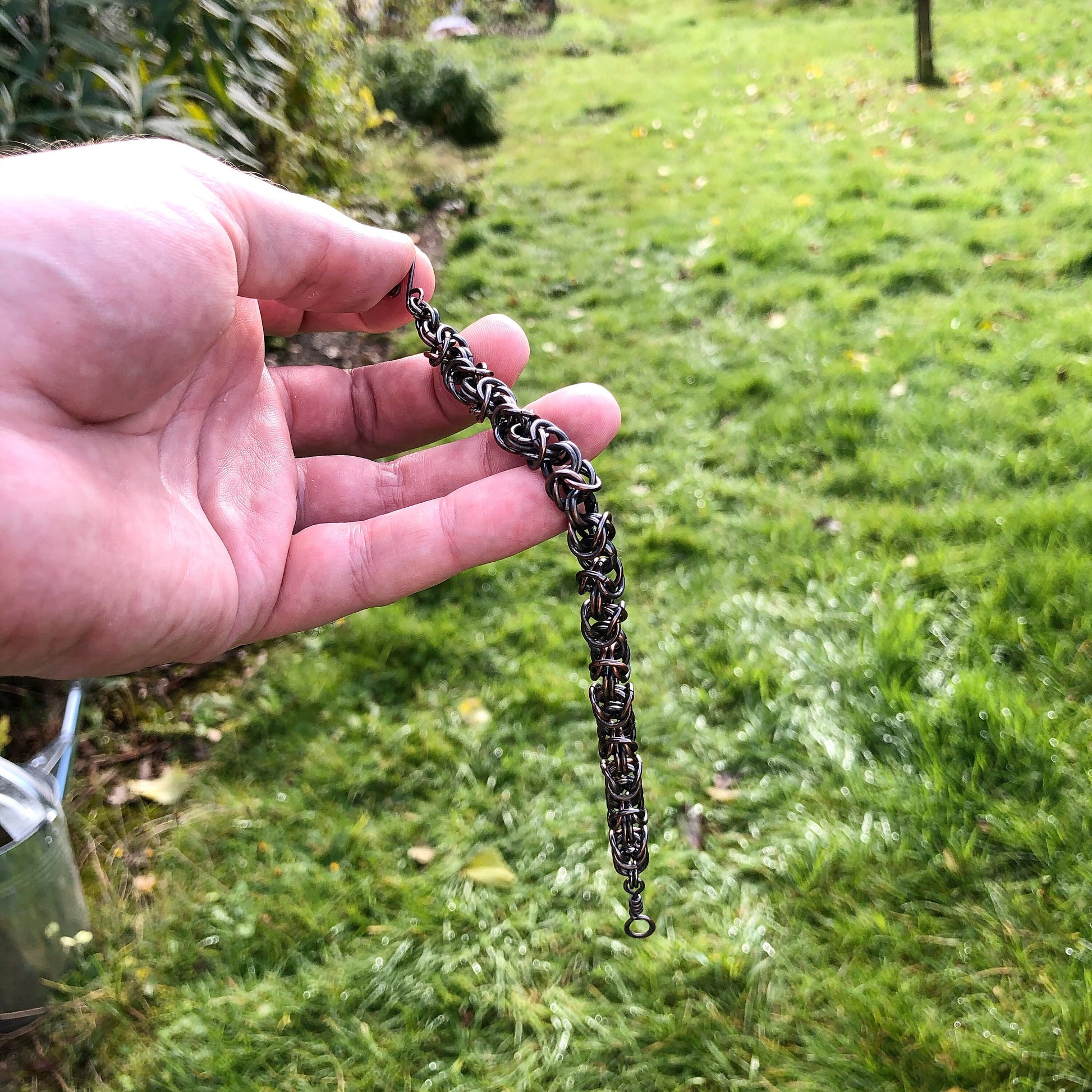 Hand holding a copper chain bracelet with a grassy background